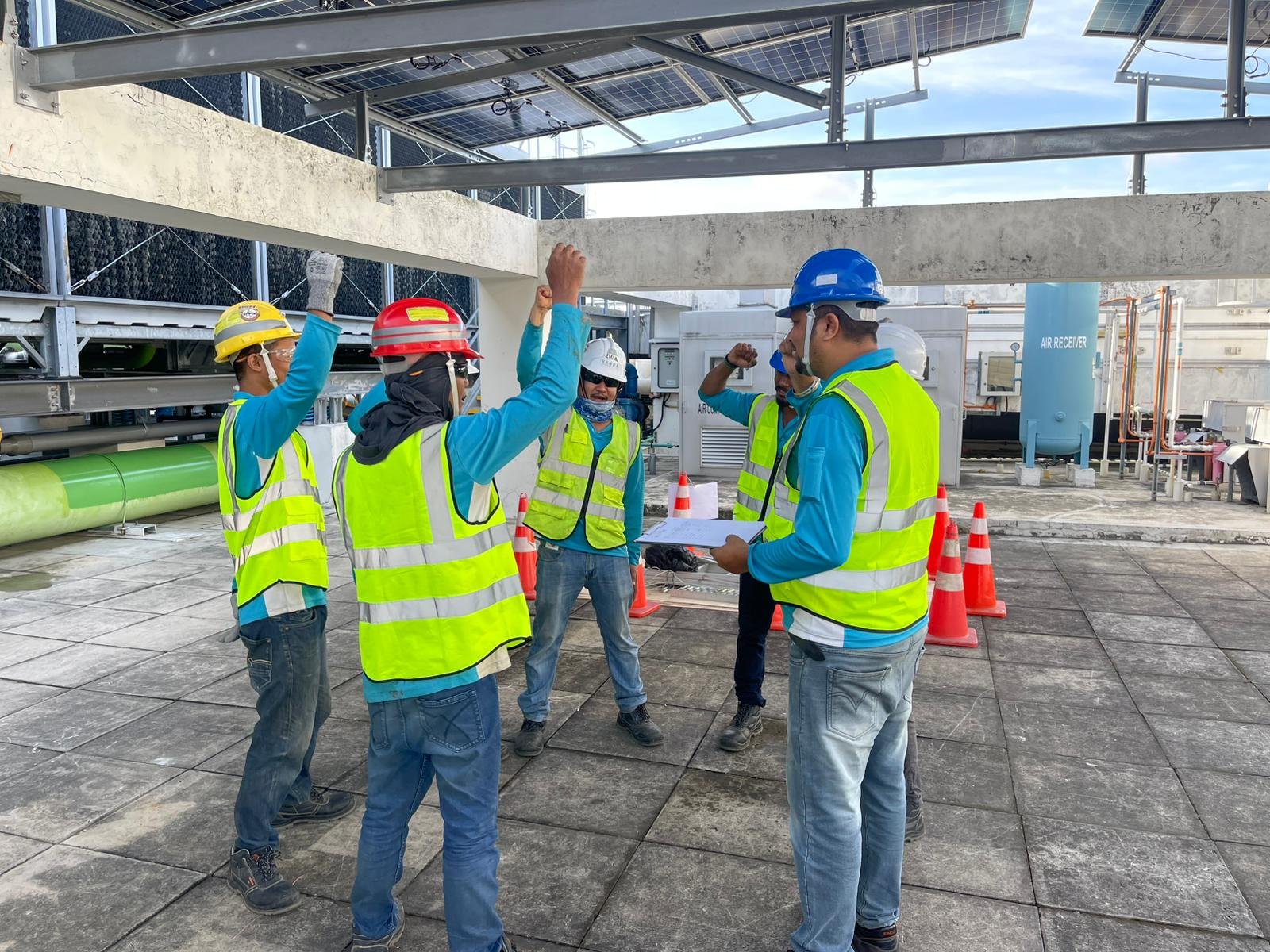 Construction workers in safety gear, including vests and helmets, holding a meeting on a rooftop with crane and equipment in the background.