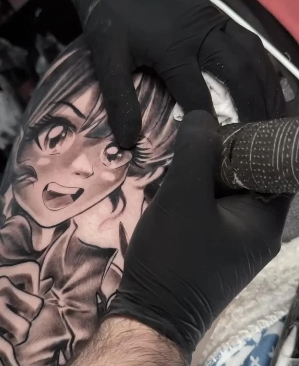 Tattoo artist working on a black and gray comic-style female face tattoo.