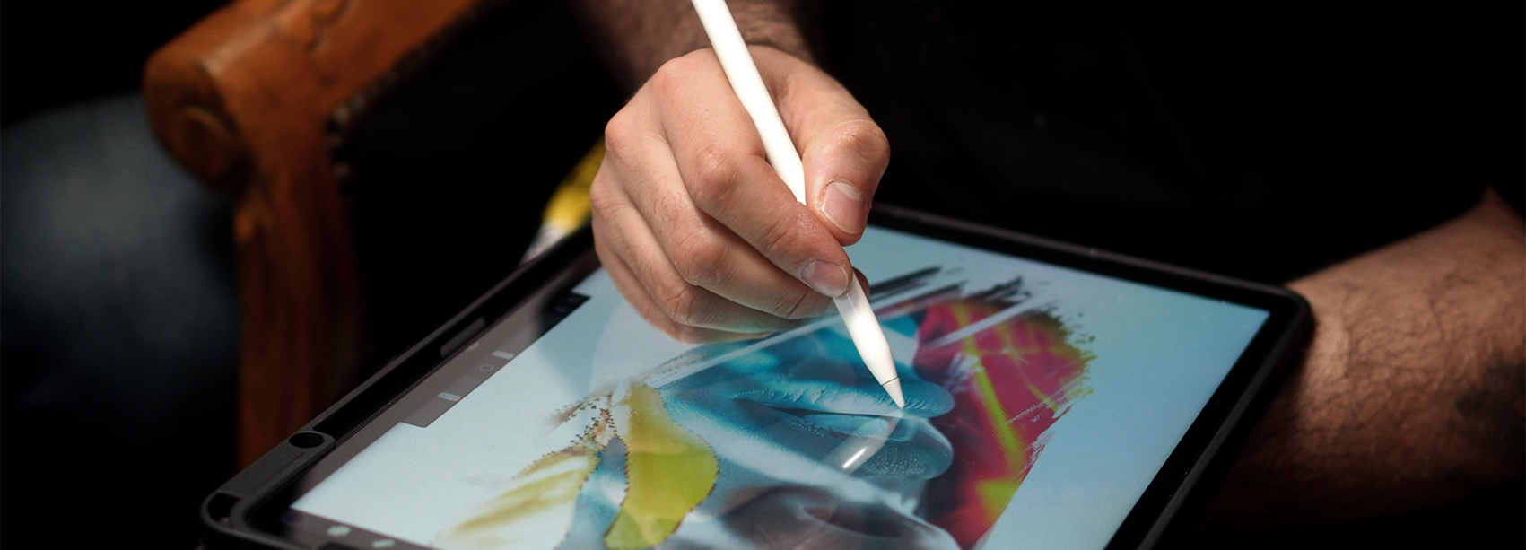 Close-up of a person's hand using a stylus to draw on a digital tablet, displaying colorful abstract art.