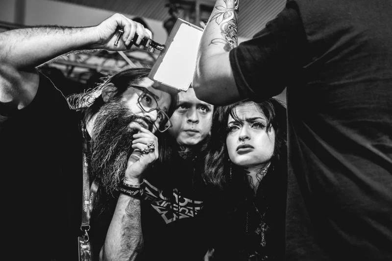 Three people look at a photo being taken, with intense expressions, in black and white.