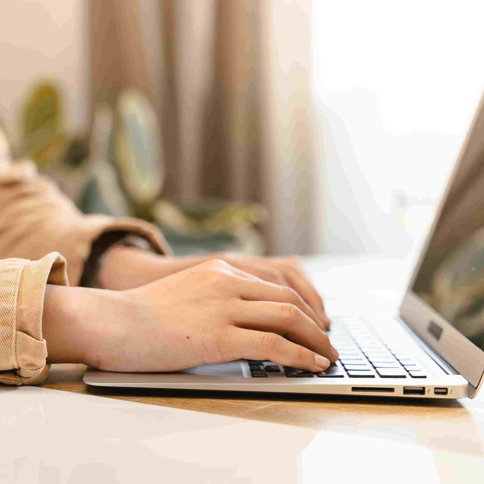 Person typing on a laptop keyboard in a well-lit room.
