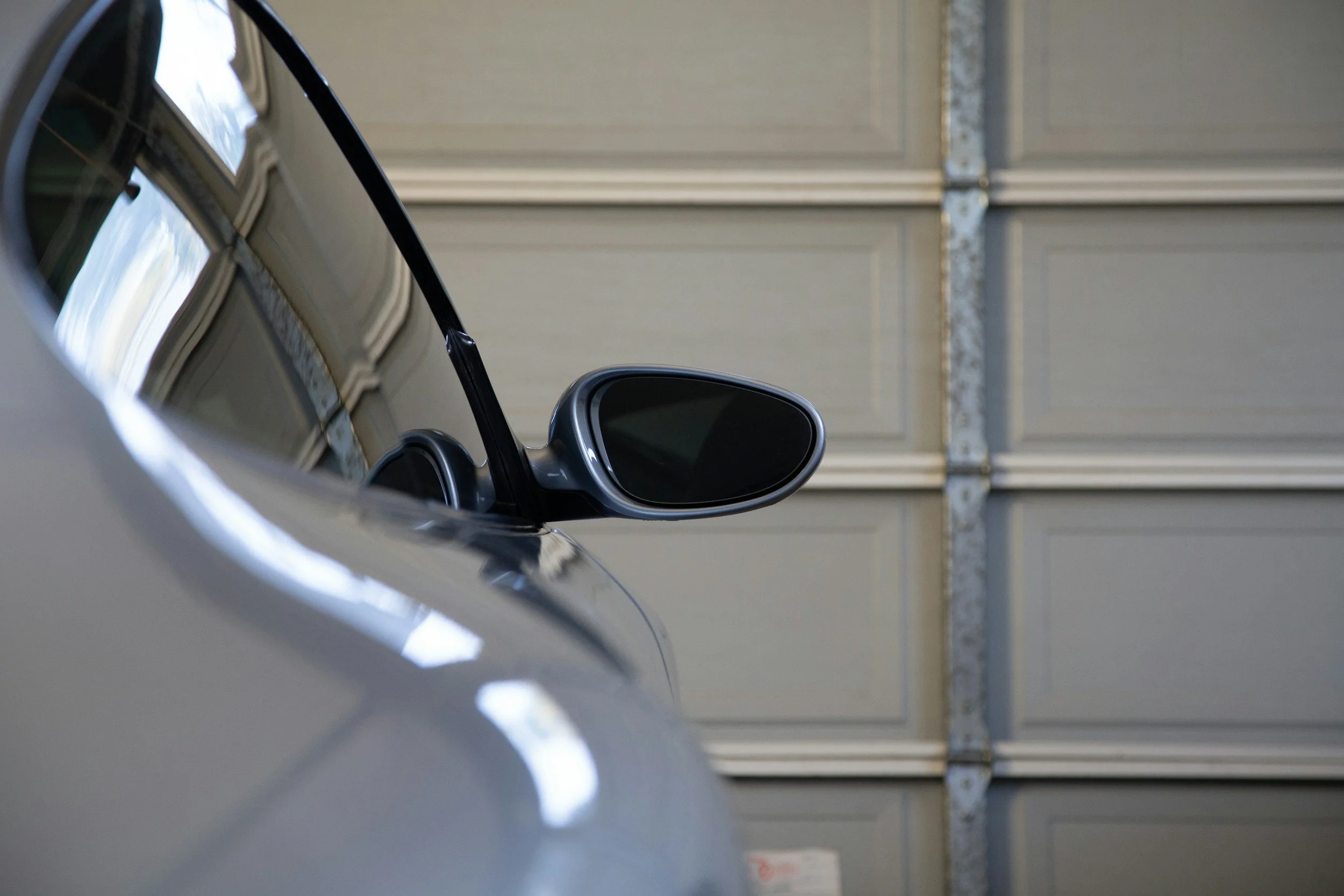 Close-up of a side mirror on a silver car parked in a garage with a closed garage door in the background.