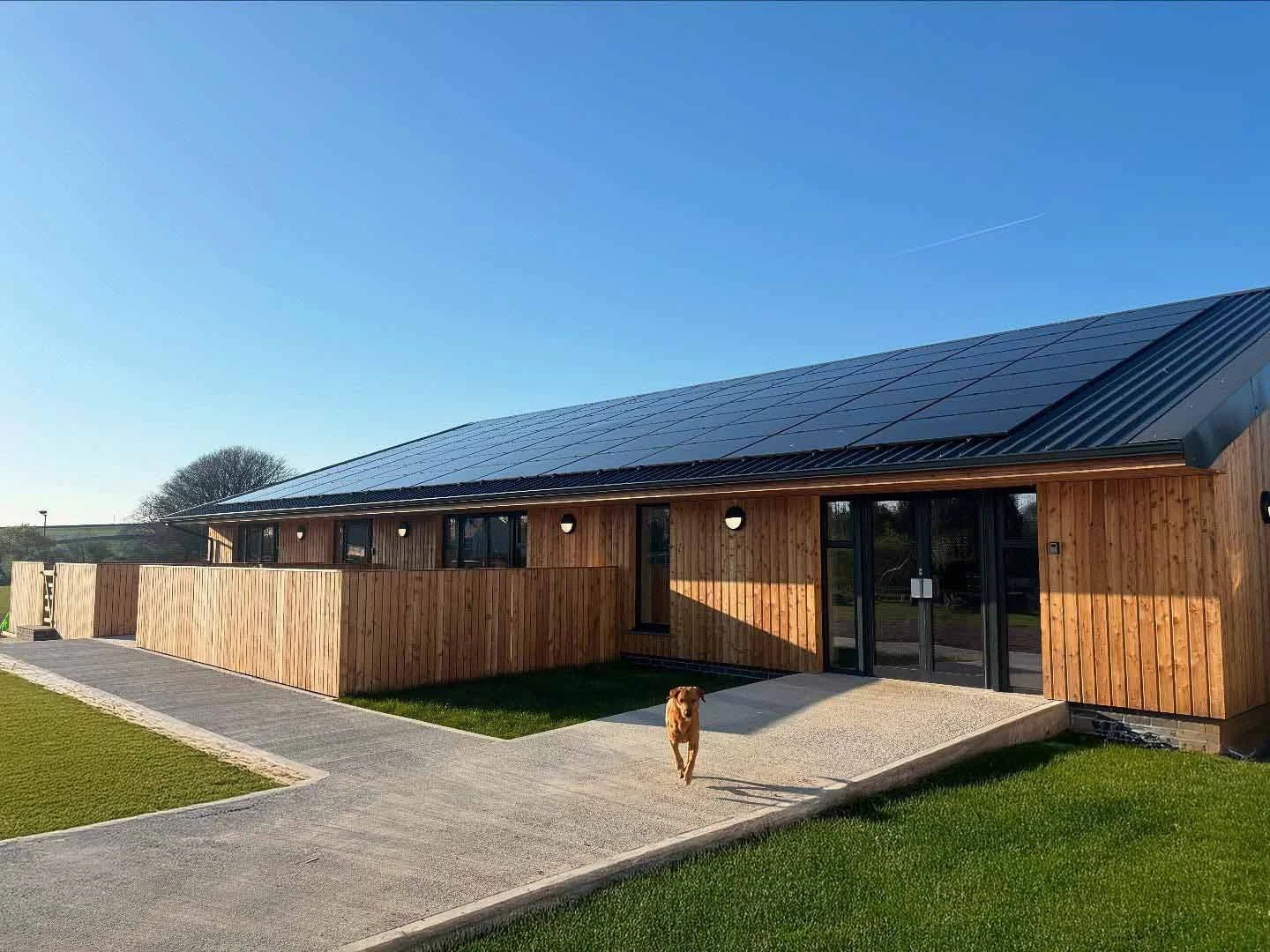 St Tudy Community Hall, Long Low Timber clad building with multiple full height windows and doors, fencing and landscaping