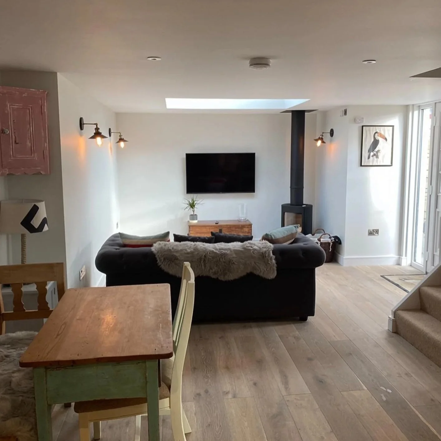 Living room extension with wood flooring, a wall-mounted TV, woodburner, skylight and french doors adds additional space to this cosy Cornish home