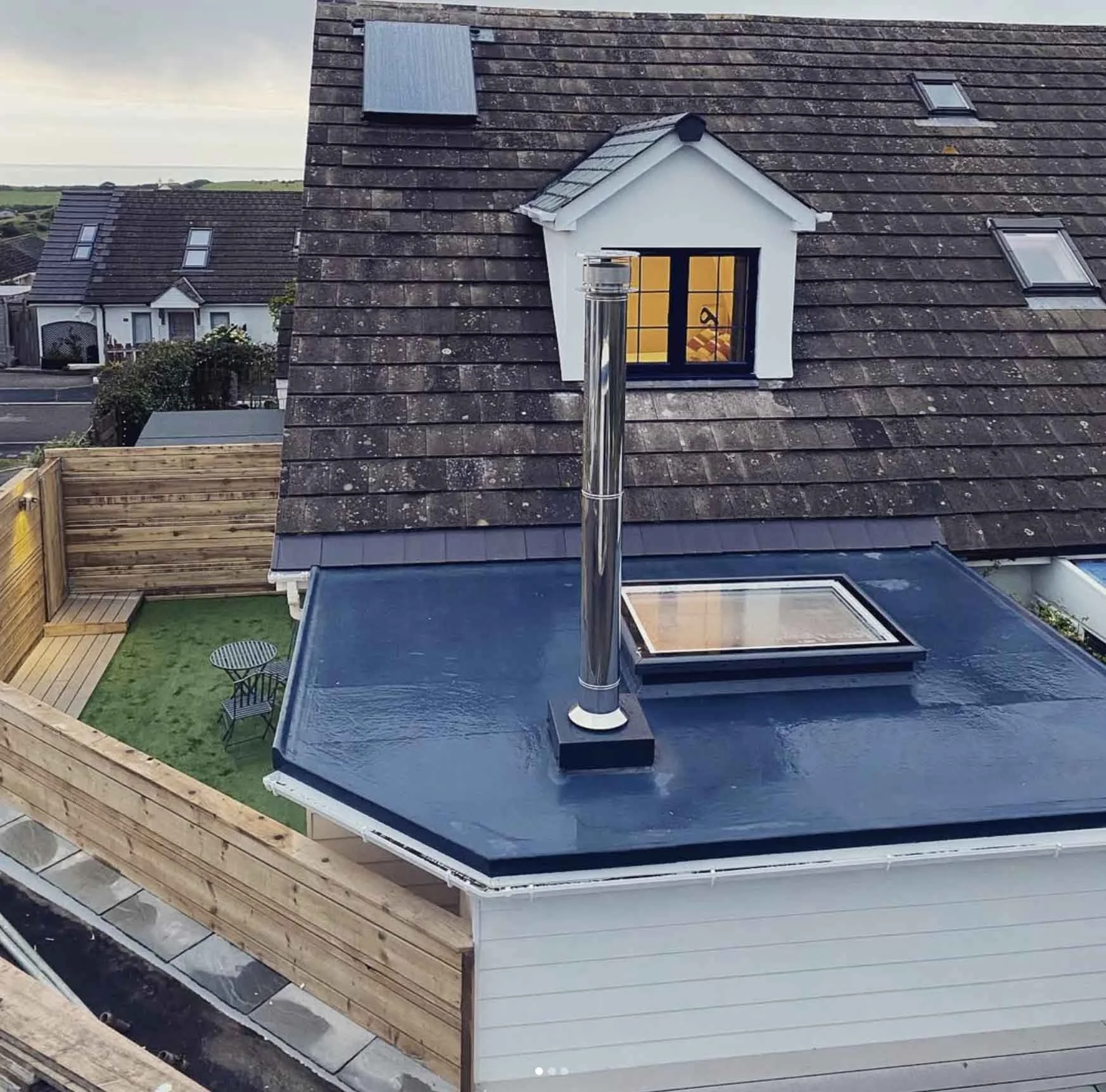 A residential rooftop showing a new skylight window and dormer window with a large blue flat roof, extension and landscaped backyard creating additional and comfortable spaces for this Cornish Home