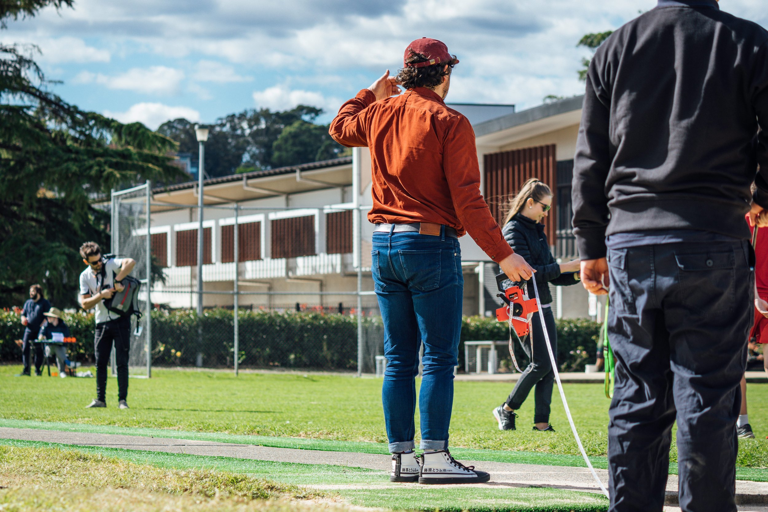 People on a field with some equipment, one person is holding a measuring device, in a sunny outdoor setting.
