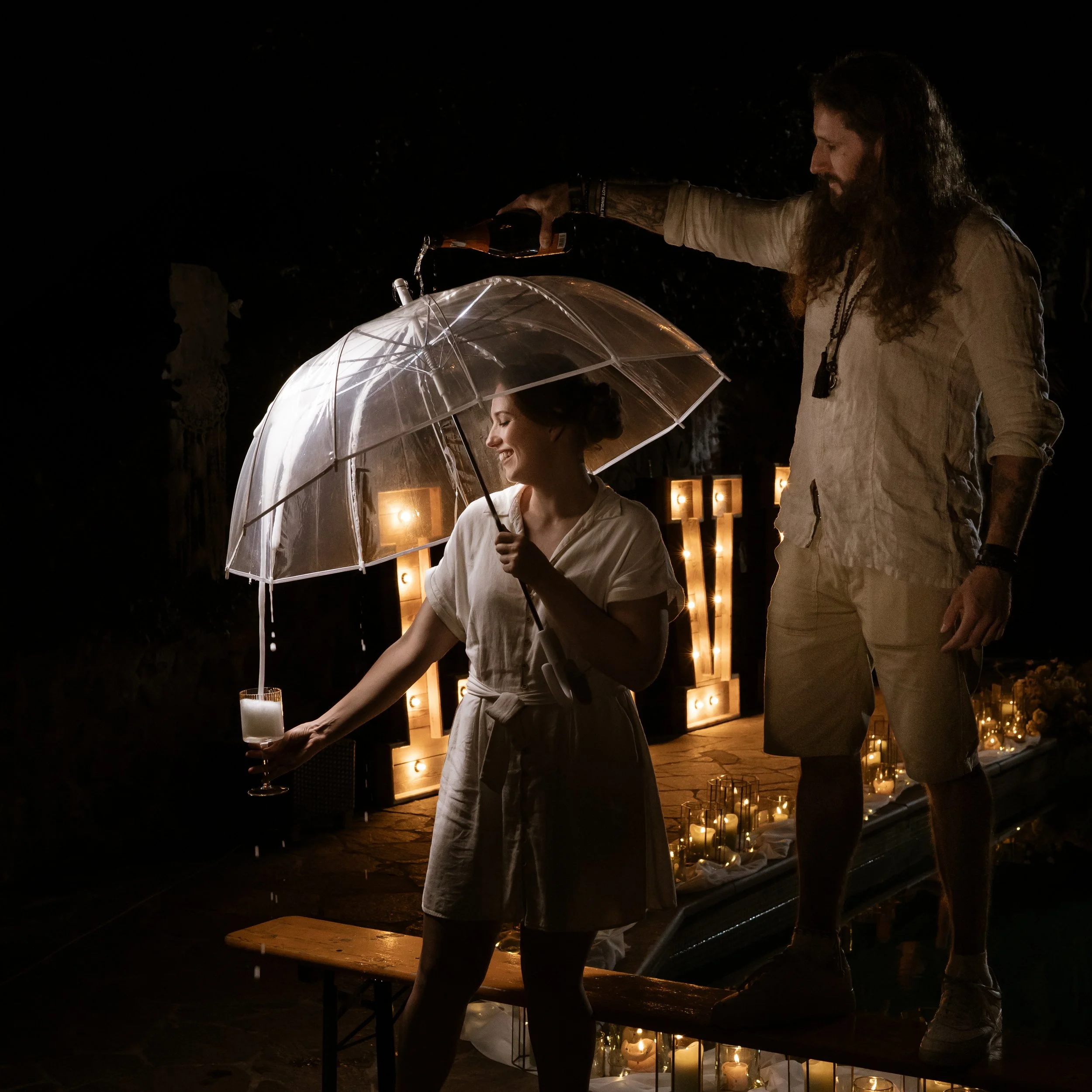 A man and woman celebrating at night, with the man holding a bottle over the woman's head to pour drink onto an umbrella she holds. portréfotózás
műtermi fotózás
glamour fotózás
divat fotózás
stúdió fotózás
kreatív fotózás
páros fotózás
rendezvény fo