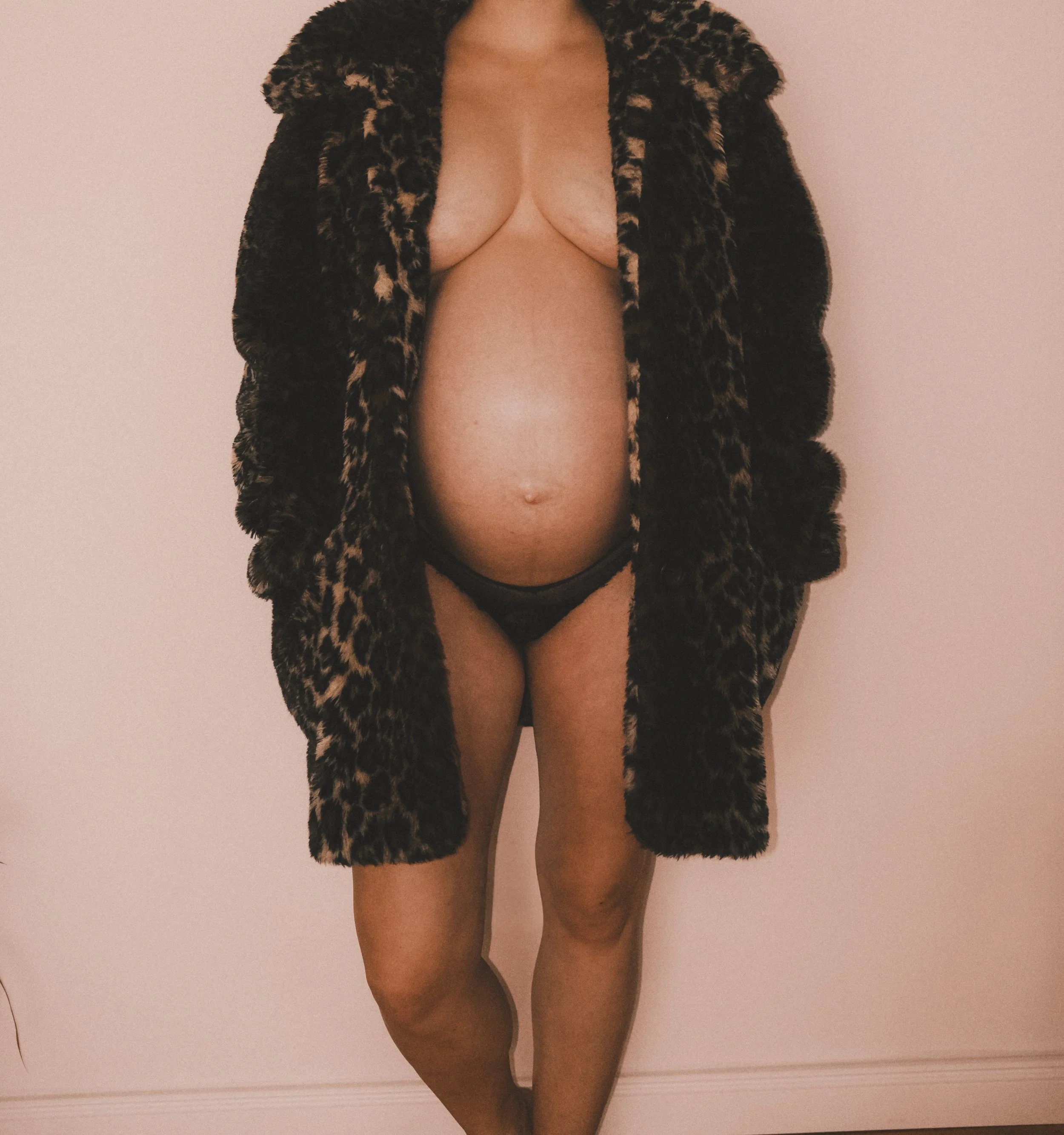 Künstlerisches Porträt einer schwangeren Frau in einem offenen Leoparden Mantel vor hellem Hintergrund – ein Bild über Körper, Stärke und werdende Mutterschaft.
