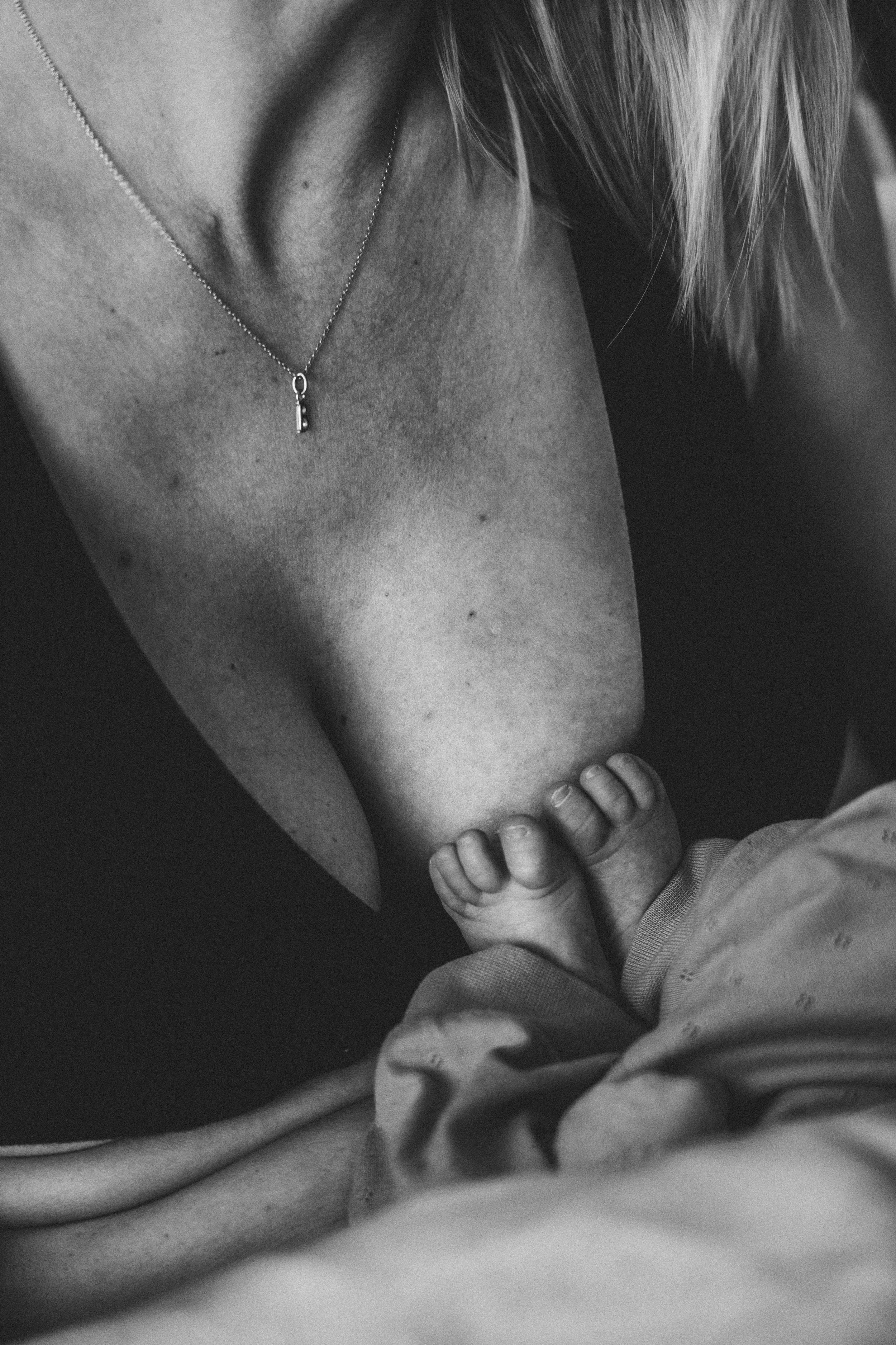 Schwarz-weiß-Foto von einer Mutter, die ihr Baby stillt, mit Fokus auf die Hand des Babys, das an der Brust der Mutter saugt.