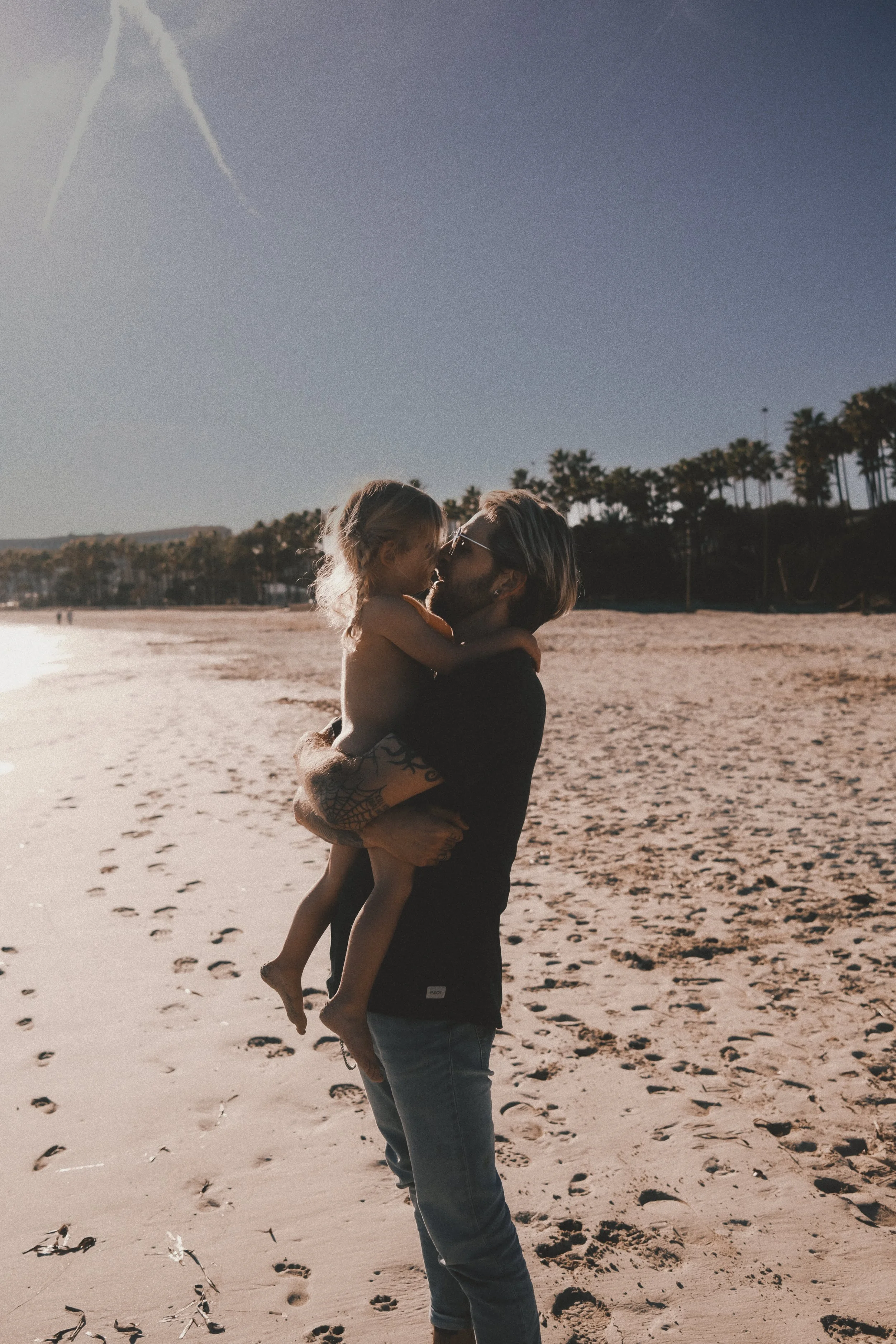 Ein Vater hält sein Kind am Strand im Arm – natürliche Familienfotografie über Nähe, Schutz und Verbundenheit.