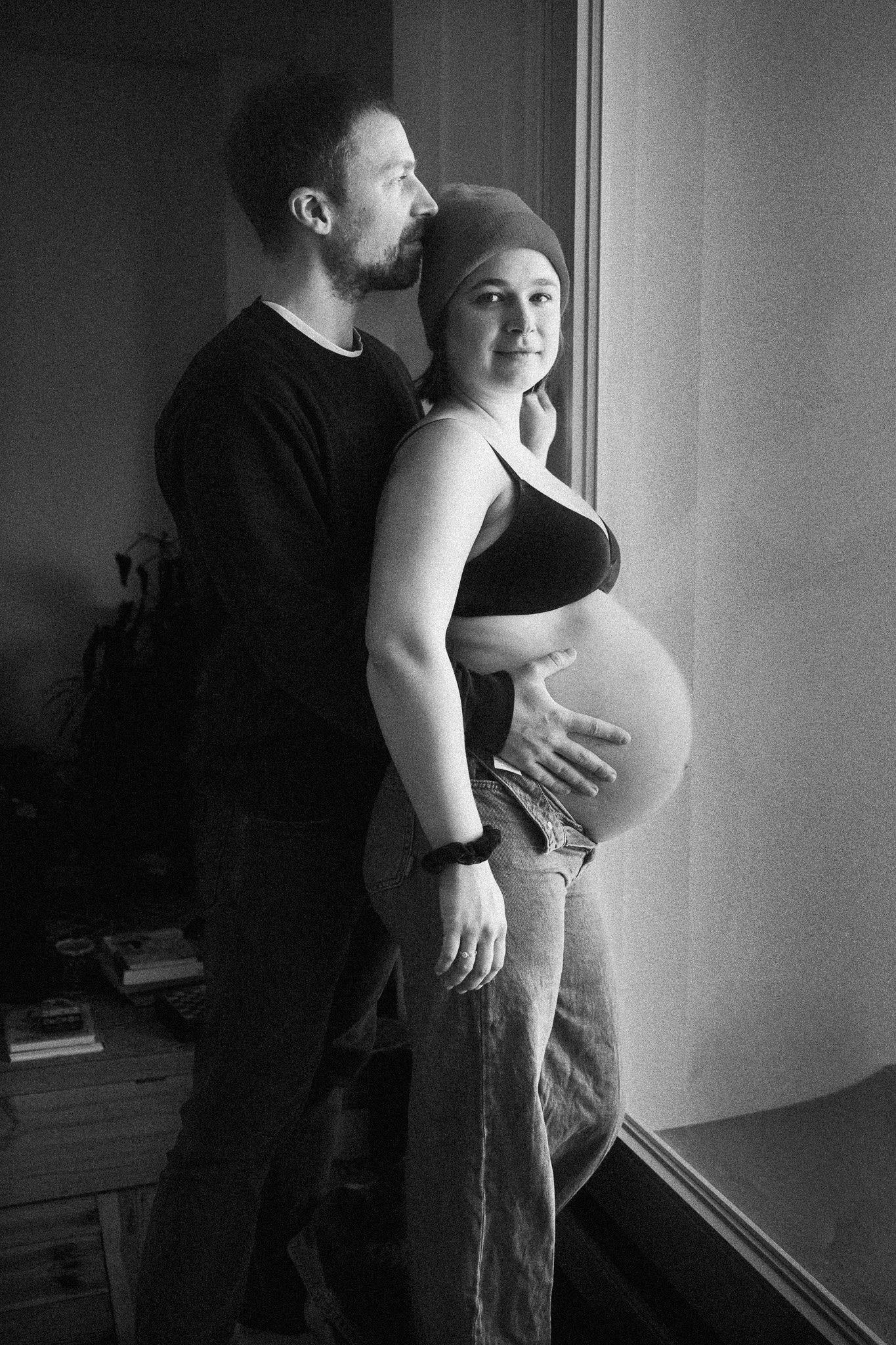 Schwarz-weiß-Porträt eines werdenden Paares am Fenster – intime Schwangerschaftsfotografie voller Nähe und Vorfreude.