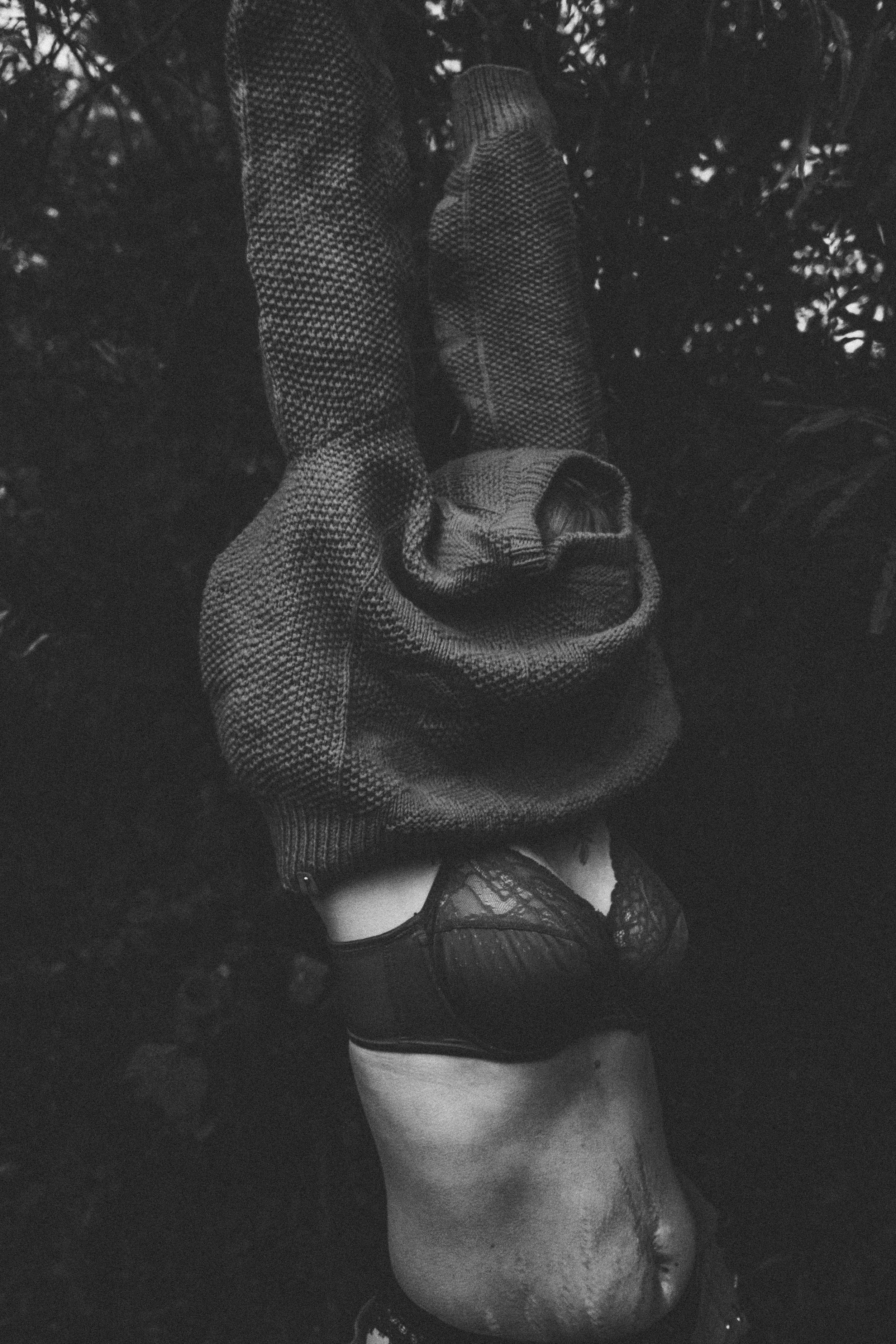 Eine Frau mit sichtbaren Narben am Bauch zieht sich in einem dunklen, ruhigen Setting einen Wollpullover über den Kopf – ein künstlerisches Porträt über Körper, Geburt und gelebte Mutterschaft.