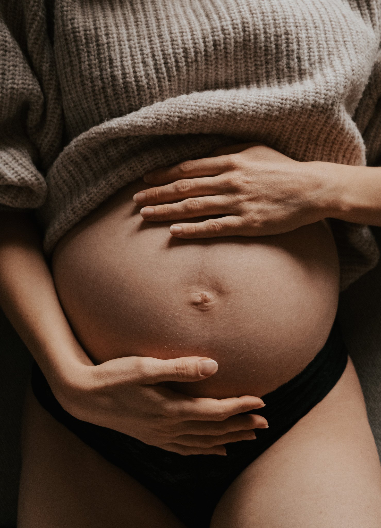 Nahaufnahme eines Babybauchs, gehalten von zwei Händen – ein Schwangerschaftsporträt über Verbundenheit und Vorfreude.