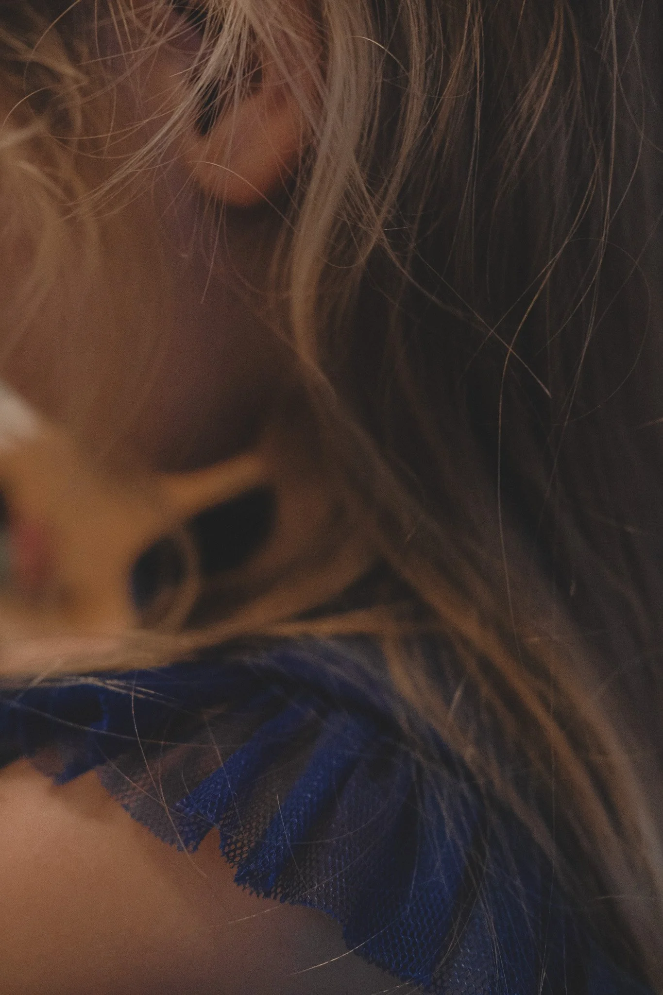 Nahaufnahme eines Mädchens mit langen Haaren und blauem Tüllrock – weiche, emotionale Kinderfotografie mit natürlichem Licht.