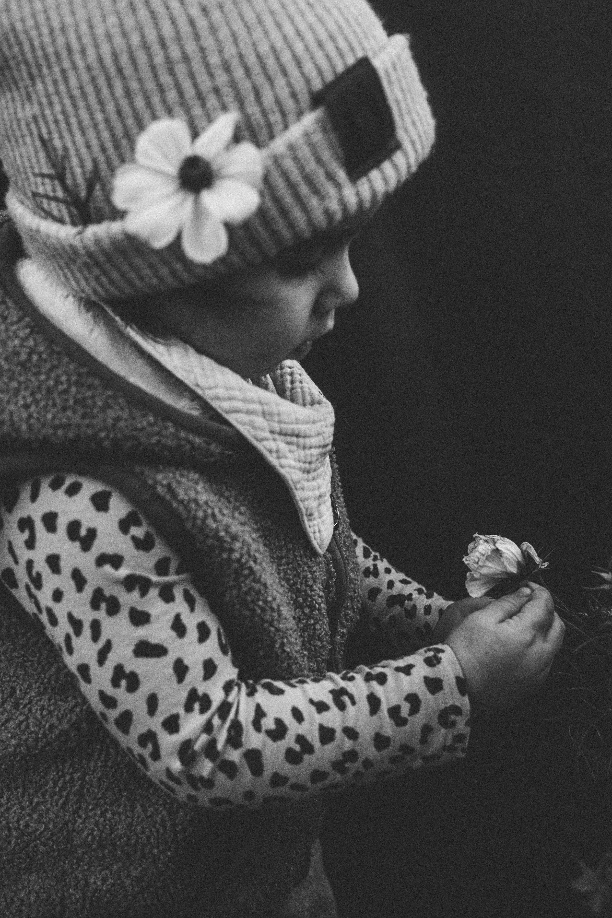 Ein Kind mit einem gestreiften Mützenhut mit einer Blumenapplikation und einem Leo-Muster-Shirt, das eine Blume hält.