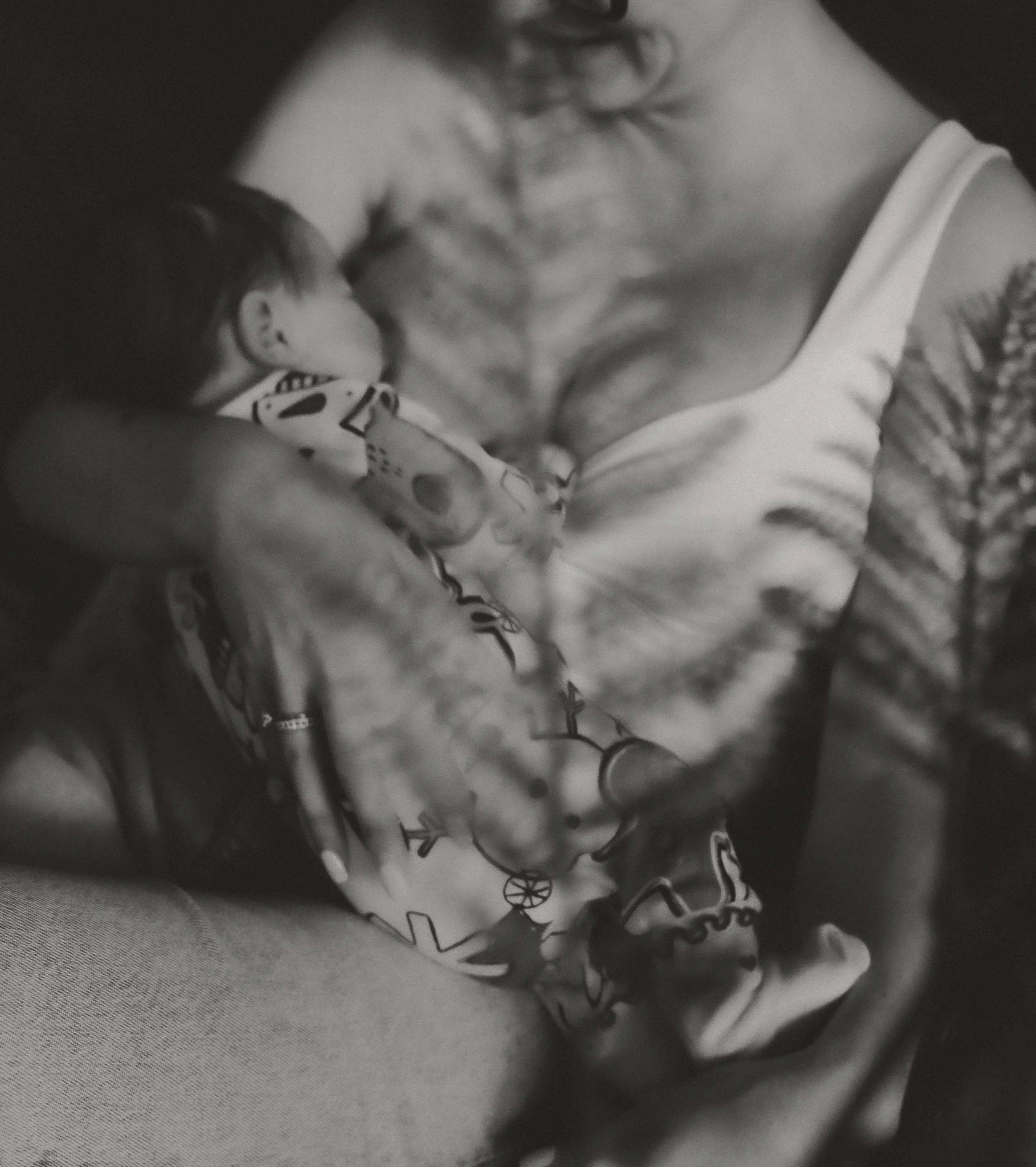 Ein kleines Kind schläft auf der Brust einer Frau, vermutlich der Mutter, in einem dunklen Raum.