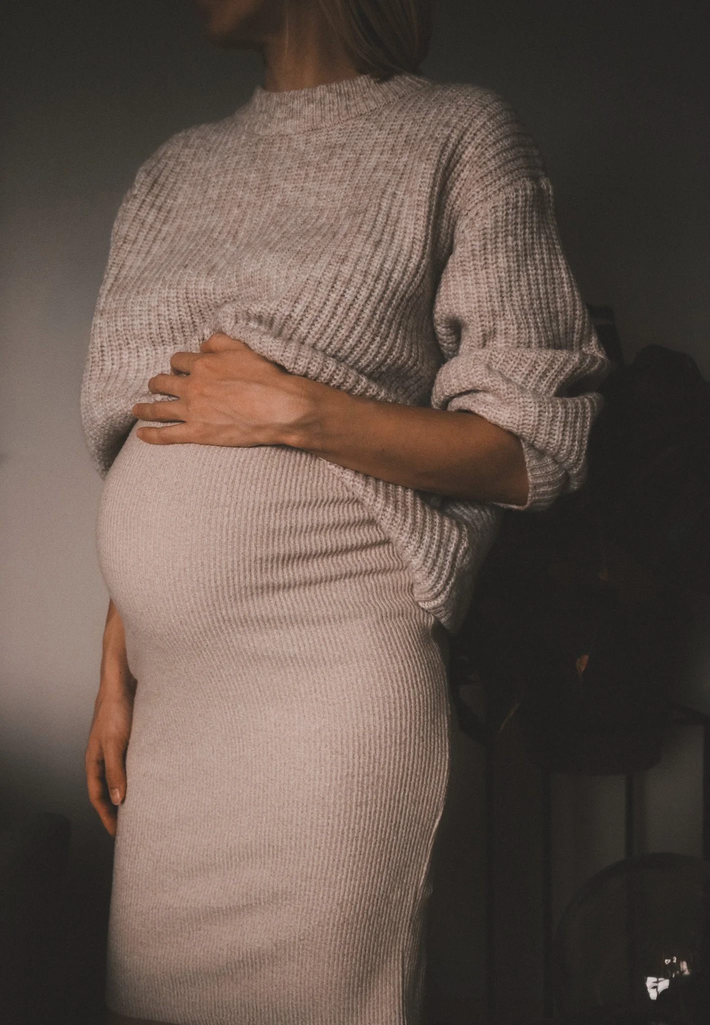 Eine schwangere Frau in einem beigen Outfit, das ihren Babybauch sanft betont – ein ruhiges Porträt aus einer Motherhood-Session.