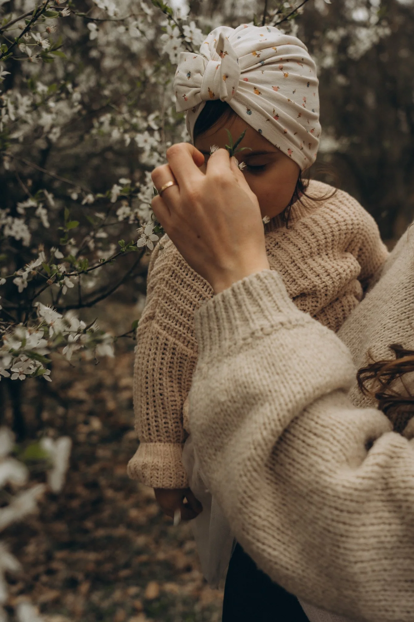 Emotionale Motherhood-Fotografie im Frühling – Mutter hält ihr Kind innig im Arm inmitten von weißen Blüten.