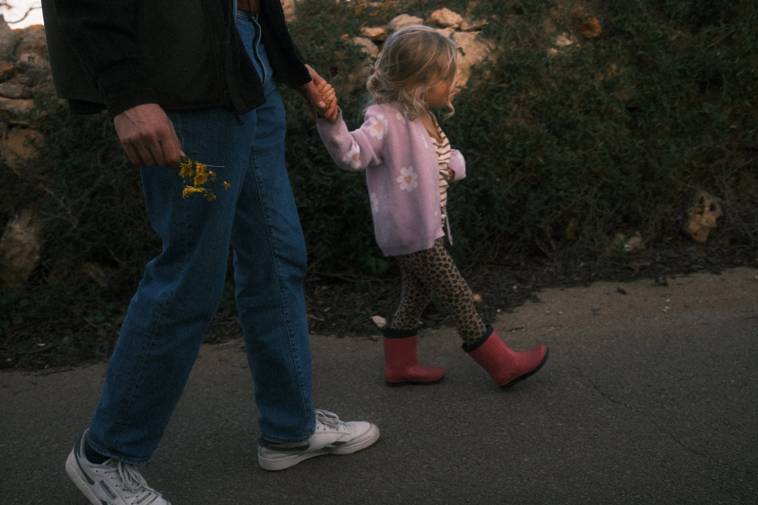 Ein Erwachsener und ein kleines Mädchen gehen Hand in Hand einen Weg entlang – liebevolle Alltagsfotografie einer Familie.