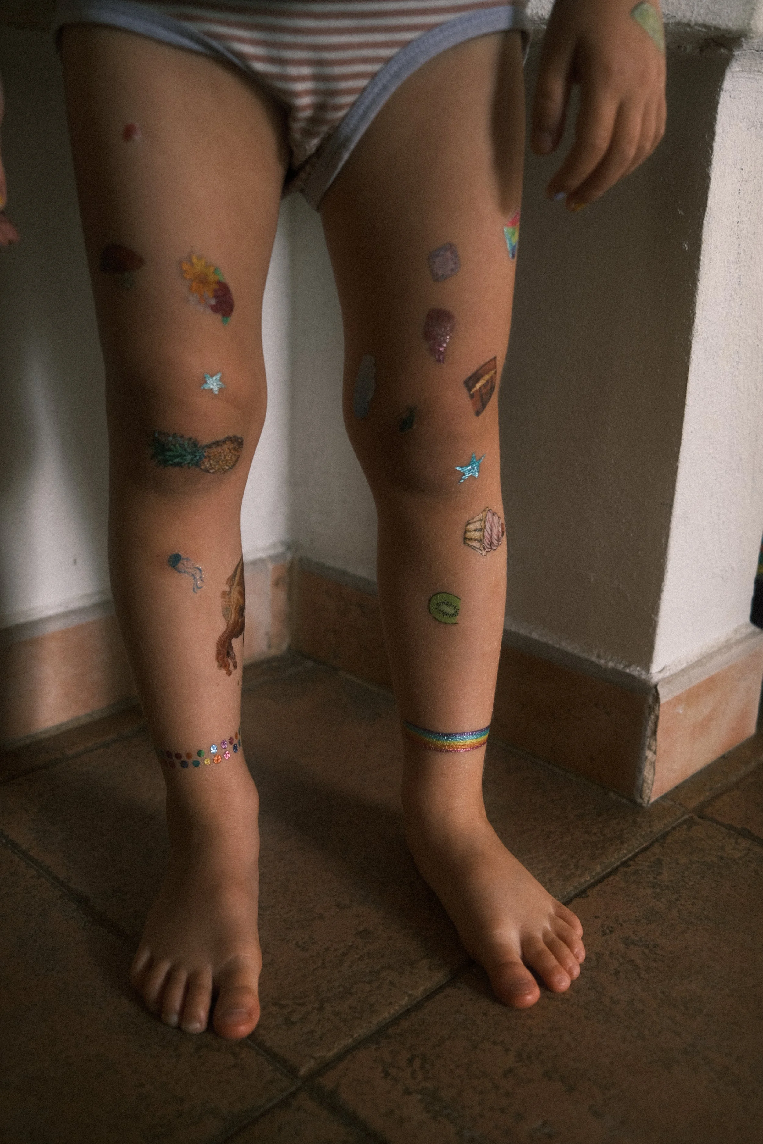 Detailaufnahme von Kinderbeinen mit bunten Klebetattoos – spielerische, echte Kindheit in einer Familienreportage.