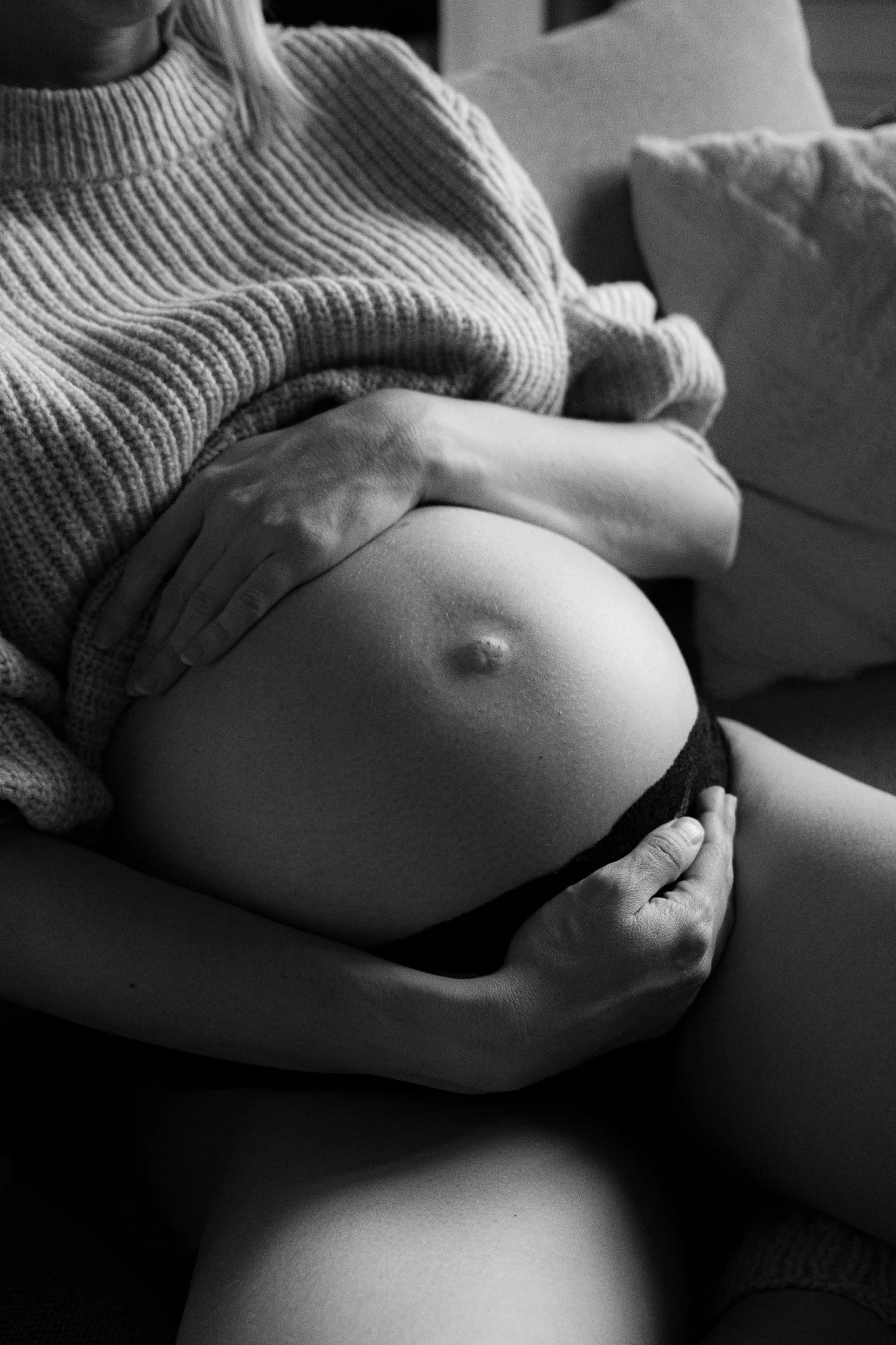 Schwarz-weiß-Porträt einer schwangeren Frau, die entspannt auf einem Sofa liegt und ihren Bauch hält – ein künstlerisches Bild über Körper, Mutterschaft und Vertrauen.