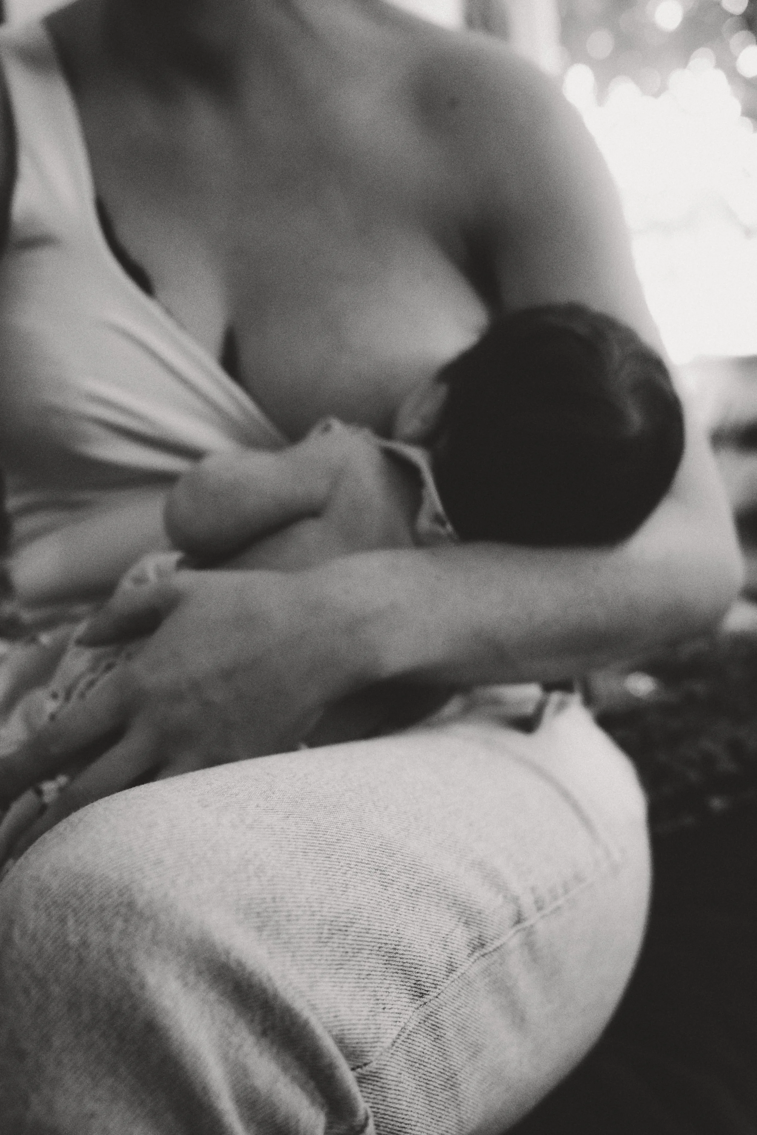 Schwarz-weiß-Fotografie einer Mutter beim Stillen ihres Babys, das in ihrem Arm liegt.