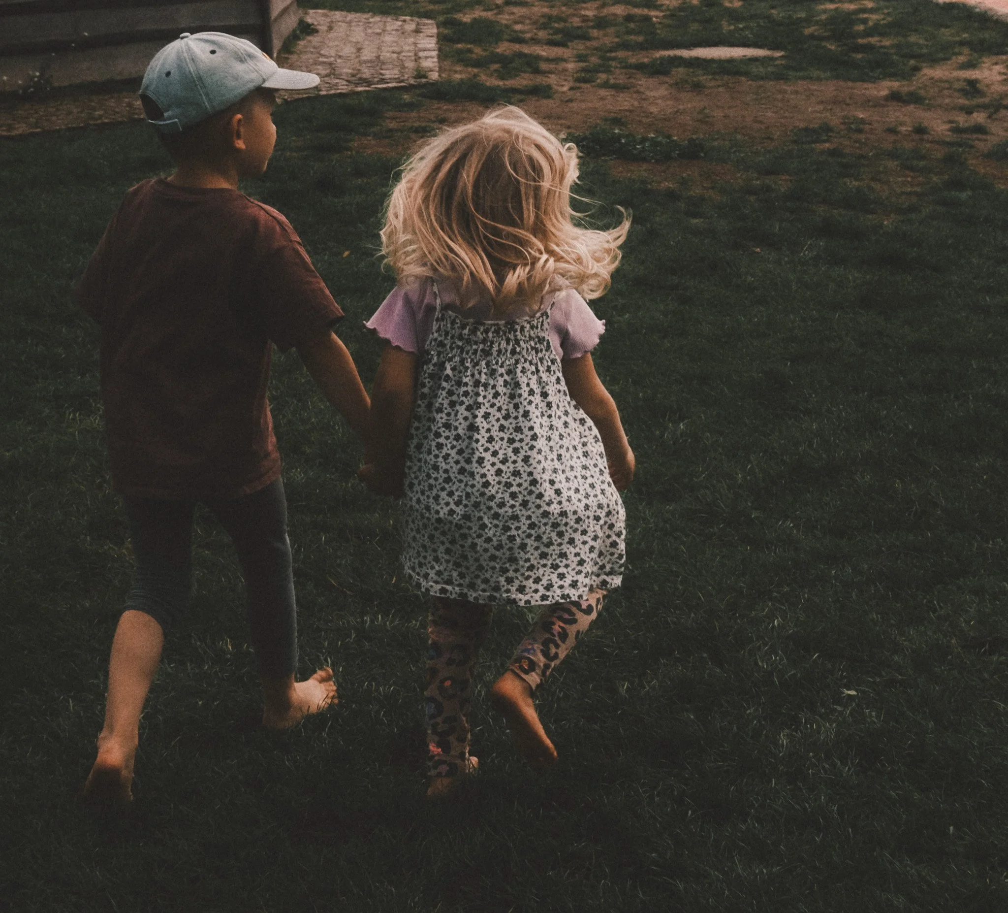 Natürliche Kinder- und Geschwisterfotografie in Berlin – zwei Kinder laufen ungestellt und Hand in Hand über eine Wiese.