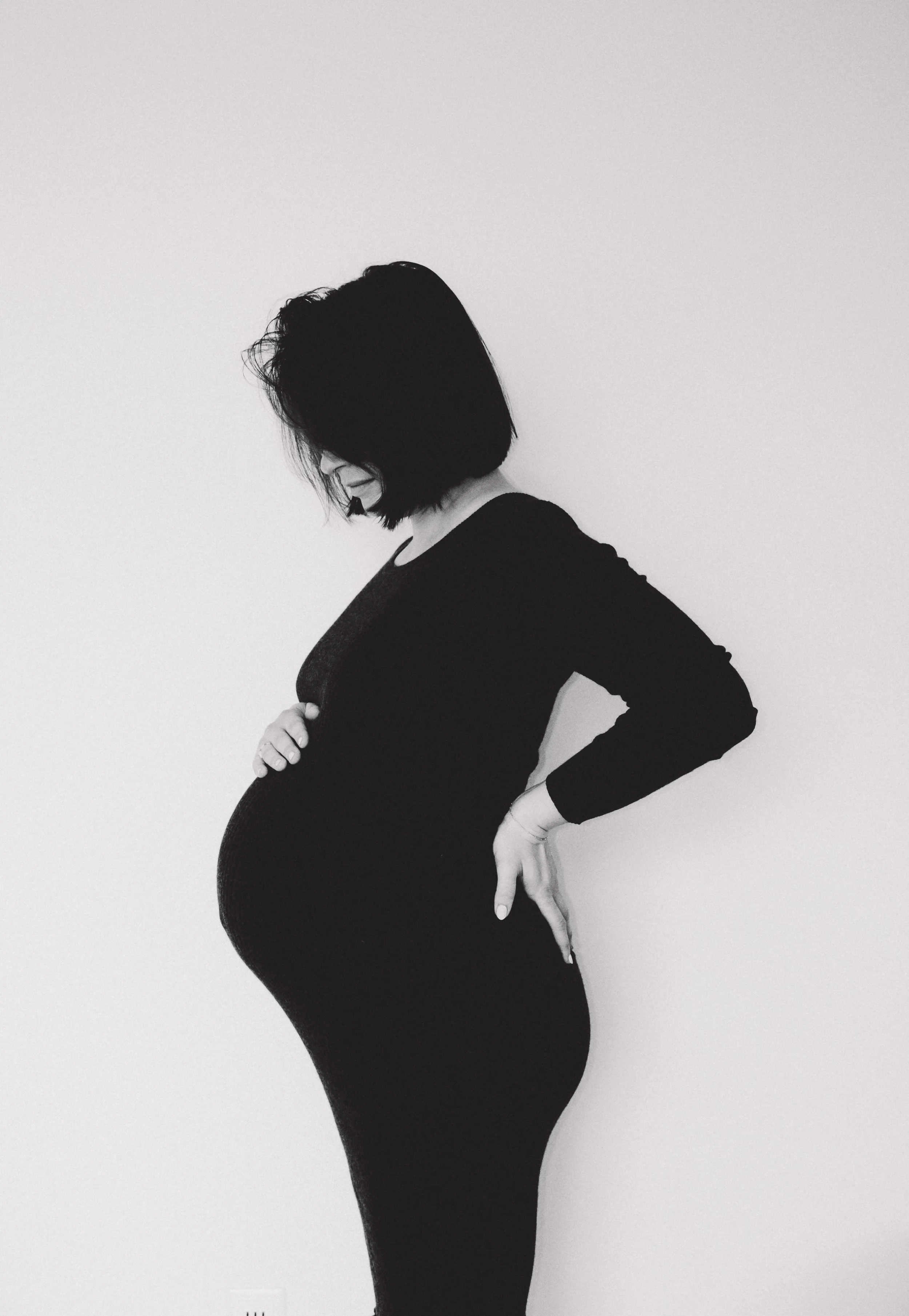 Schwarz-weiß-Porträt einer schwangeren Frau, die ruhig auf ihren Babybauch blickt – ein stilles Bild über Vorfreude und werdende Mutterschaft. Analoges Bild