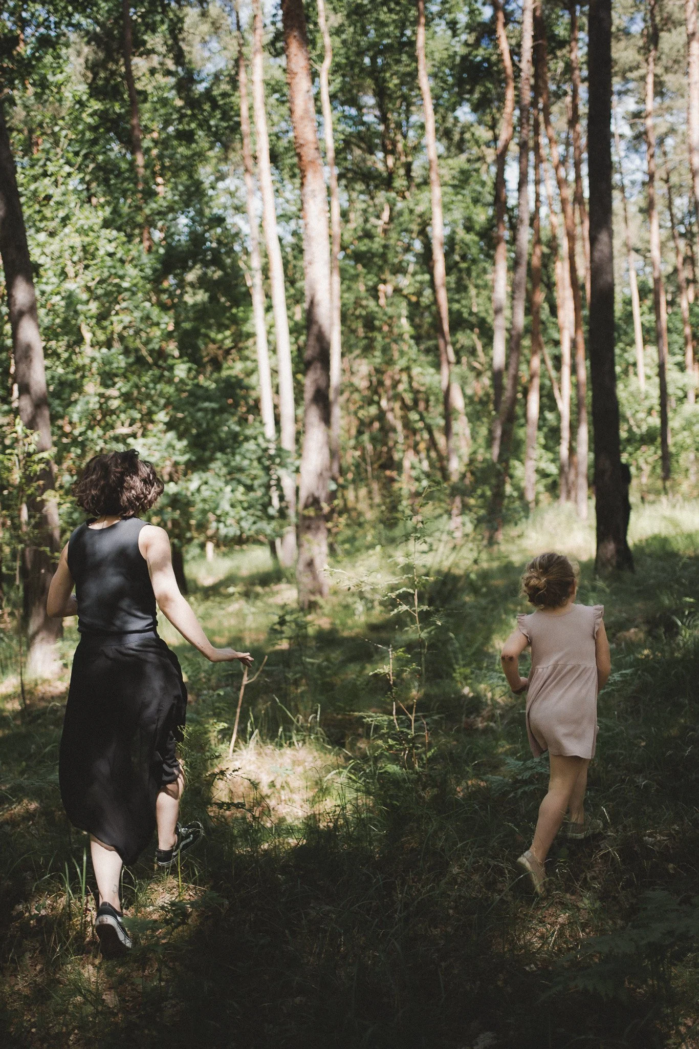 Natürliche Motherhood- und Familienfotografie Brandenburg – Mutter und Tochter laufen Hand in Hand durch einen lichten Wald.