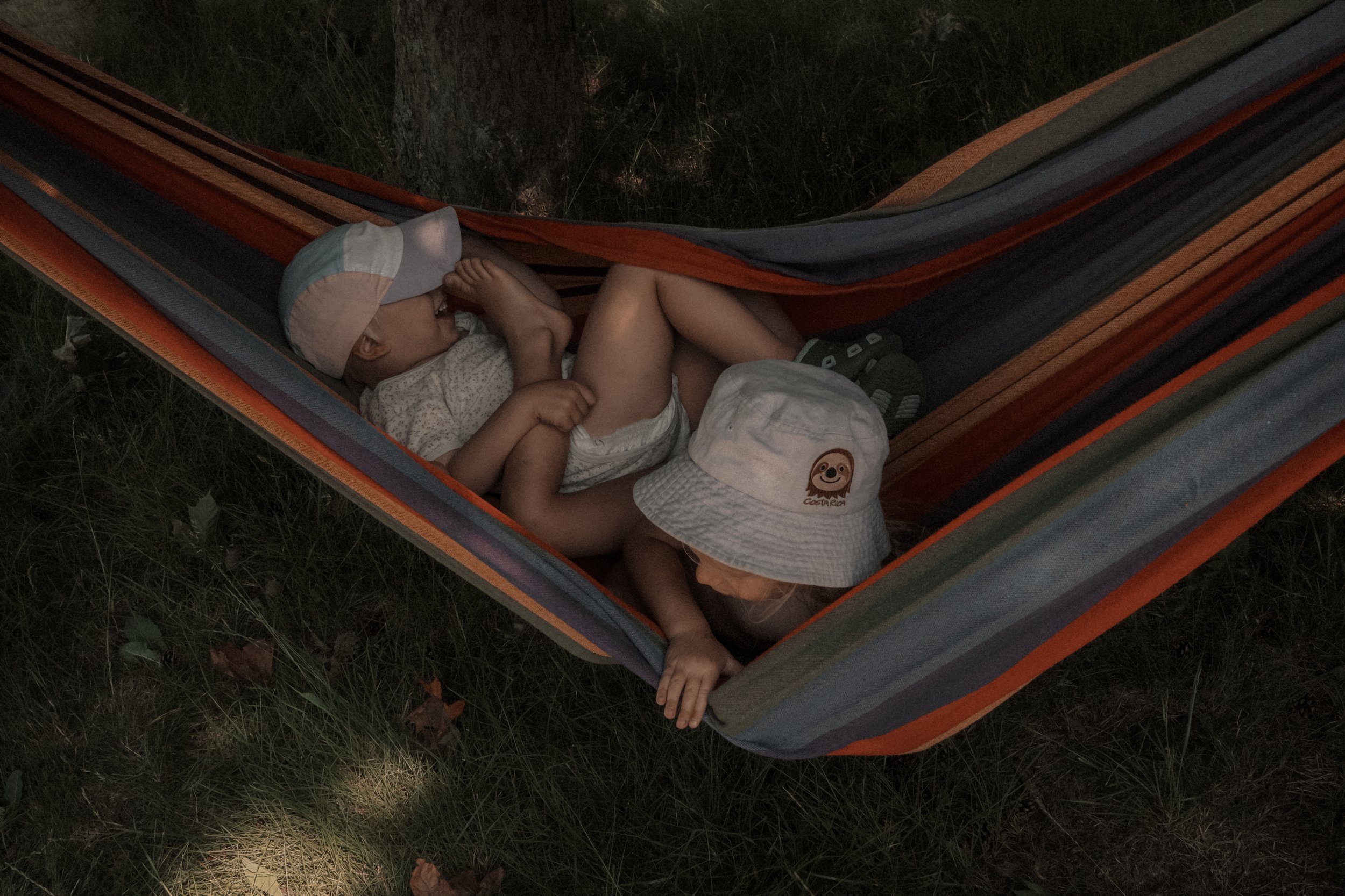 Zwei Kinder schlafen eng aneinander in einer bunten Hängematte im Garten – ruhige, authentische Familienfotografie voller Geborgenheit.