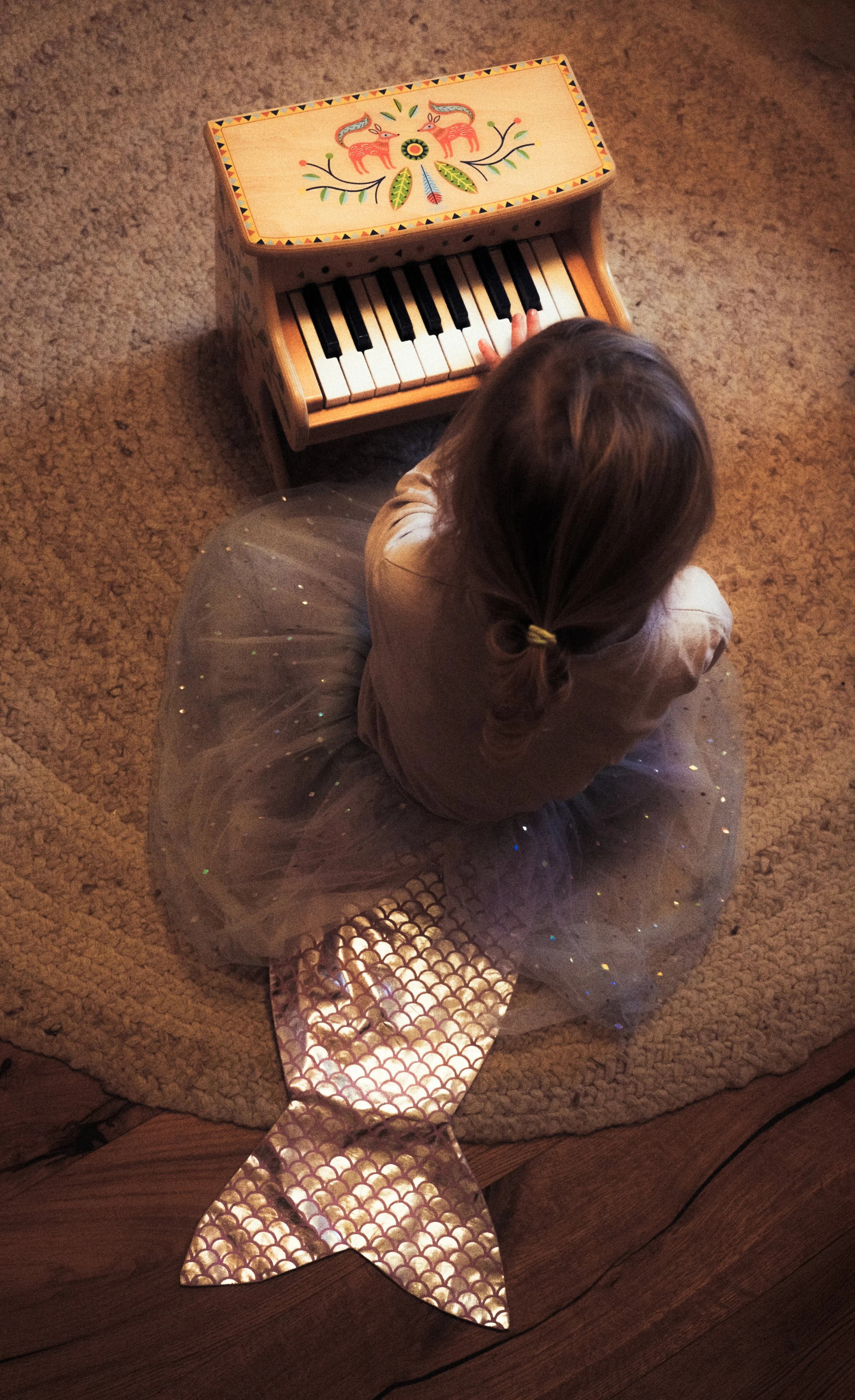 Ein kleines Mädchen sitzt mit Spielzeugflügeln auf dem Boden – liebevolle Kinderfotografie voller Fantasie und ruhiger Momente.