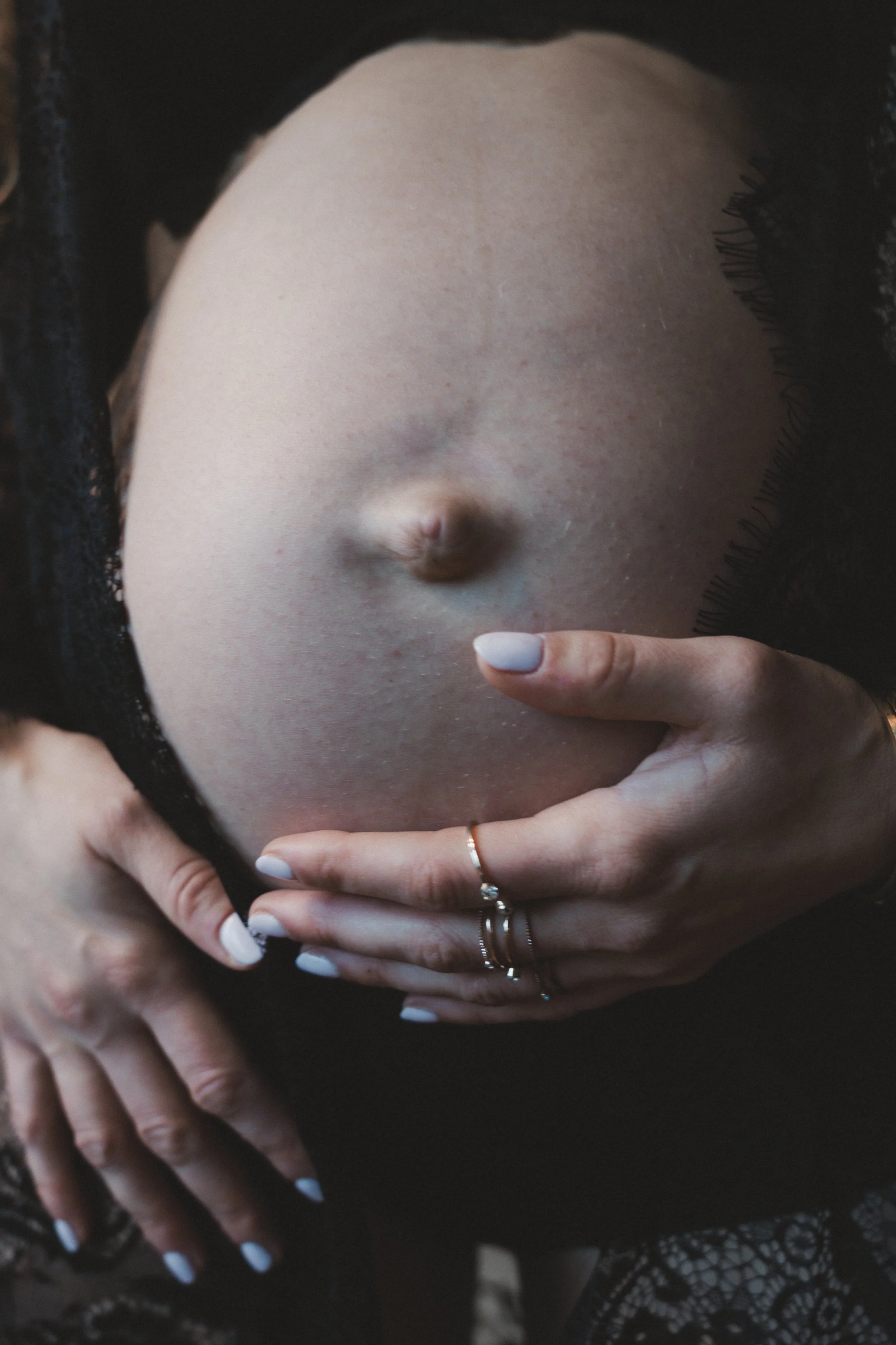 Nahaufnahme eines Babybauchs, gehalten von zwei Händen – ein künstlerisches Schwangerschaftsporträt über Schutz, Nähe und neues Leben.