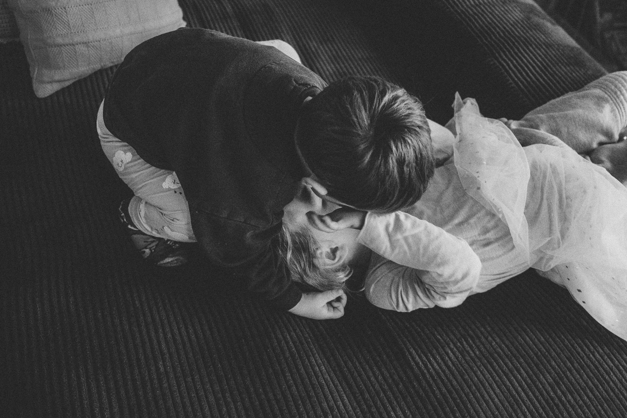 Zwei Kinder kuscheln sich auf einem Sofa aneinander – ein warmes Schwarz-weiß-Porträt über Nähe und Geschwisterliebe.