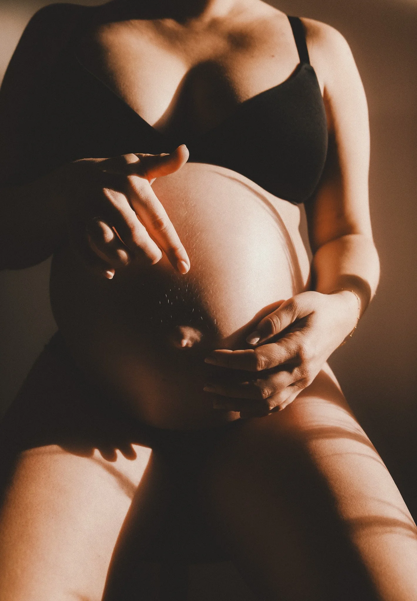 Künstlerisches Schwangerschaftsporträt einer werdenden Mutter, die ihren Bauch mit beiden Händen hält – ein kraftvolles Bild über Körper, Selbstbestimmung und neues Leben.