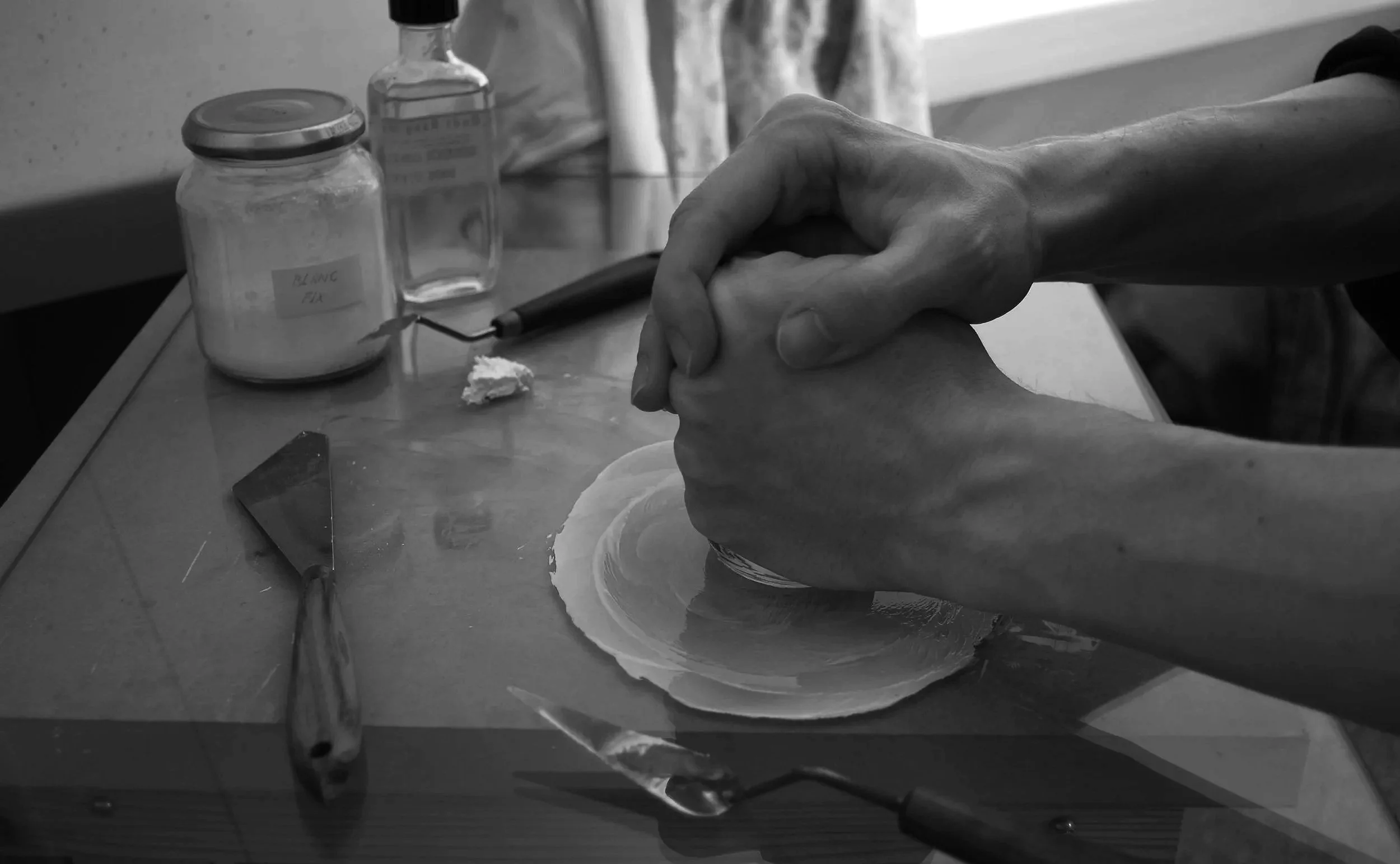 Een kunstenaar, Sietse Jonker, wrijft zijn verf met pigmenten, olie, schilder mes en wrijfloper op een glazen plaat.