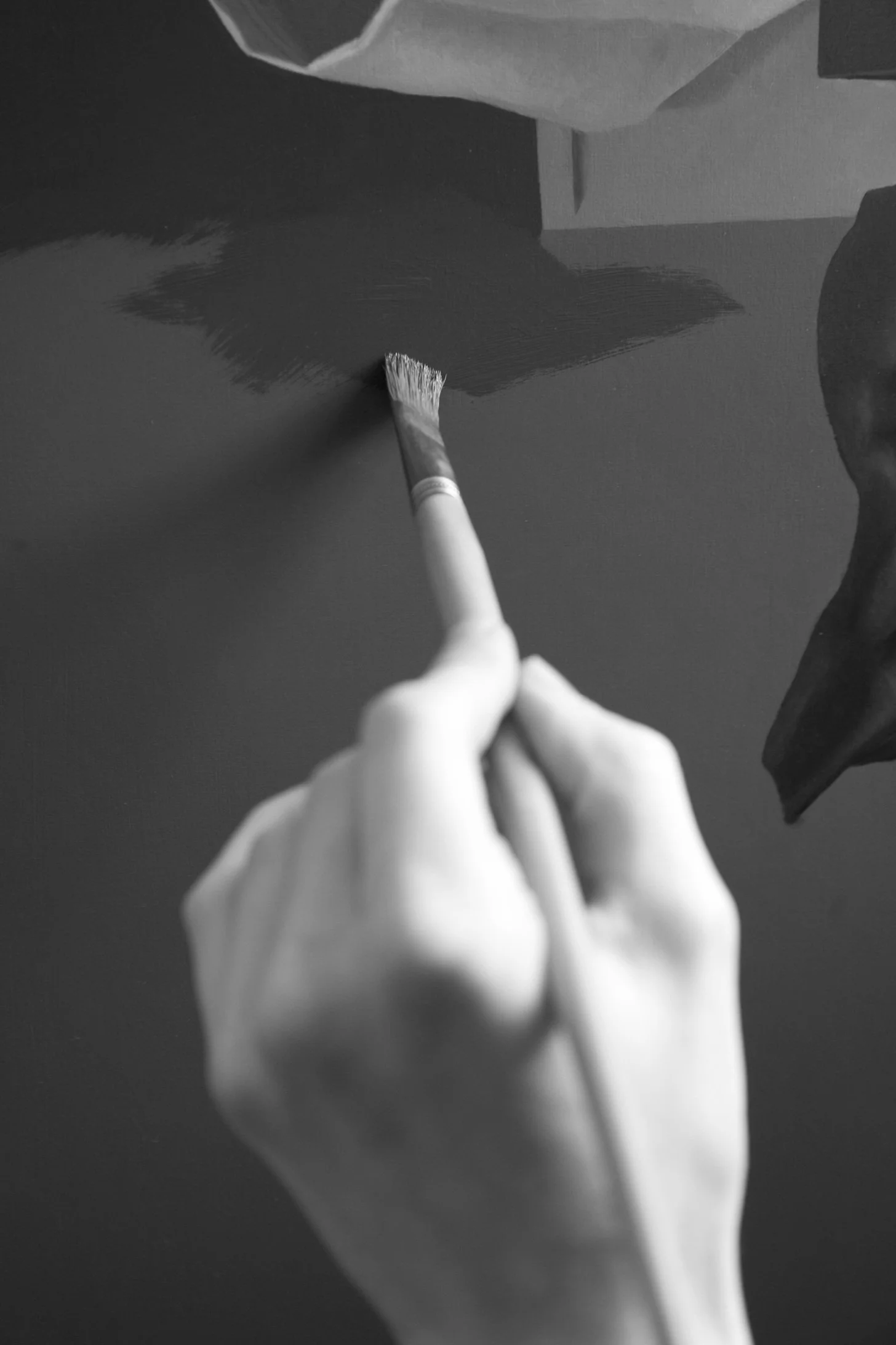 Zwart-wit foto van een hand die een verfkwast vasthoudt en een muur schildert.