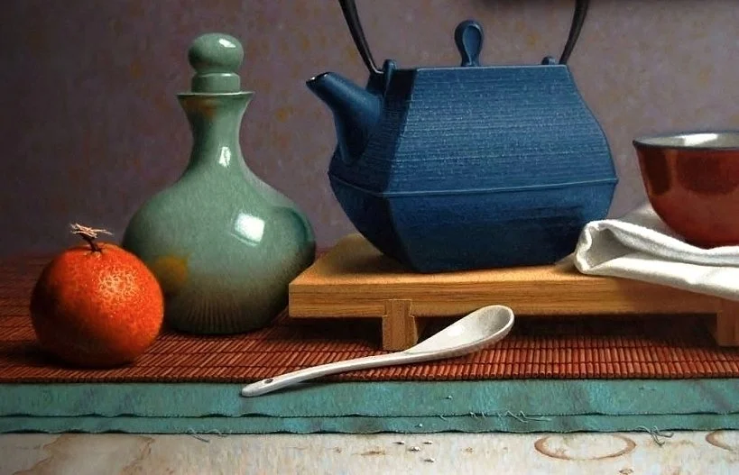 Een thee- en serveerset met een groene kruik, een blauwe theepot, een roodachtige kom, een witte lepel en een witte doek op een houten onderblad, geplaatst op een tafel met een gekleurde tafelmat.