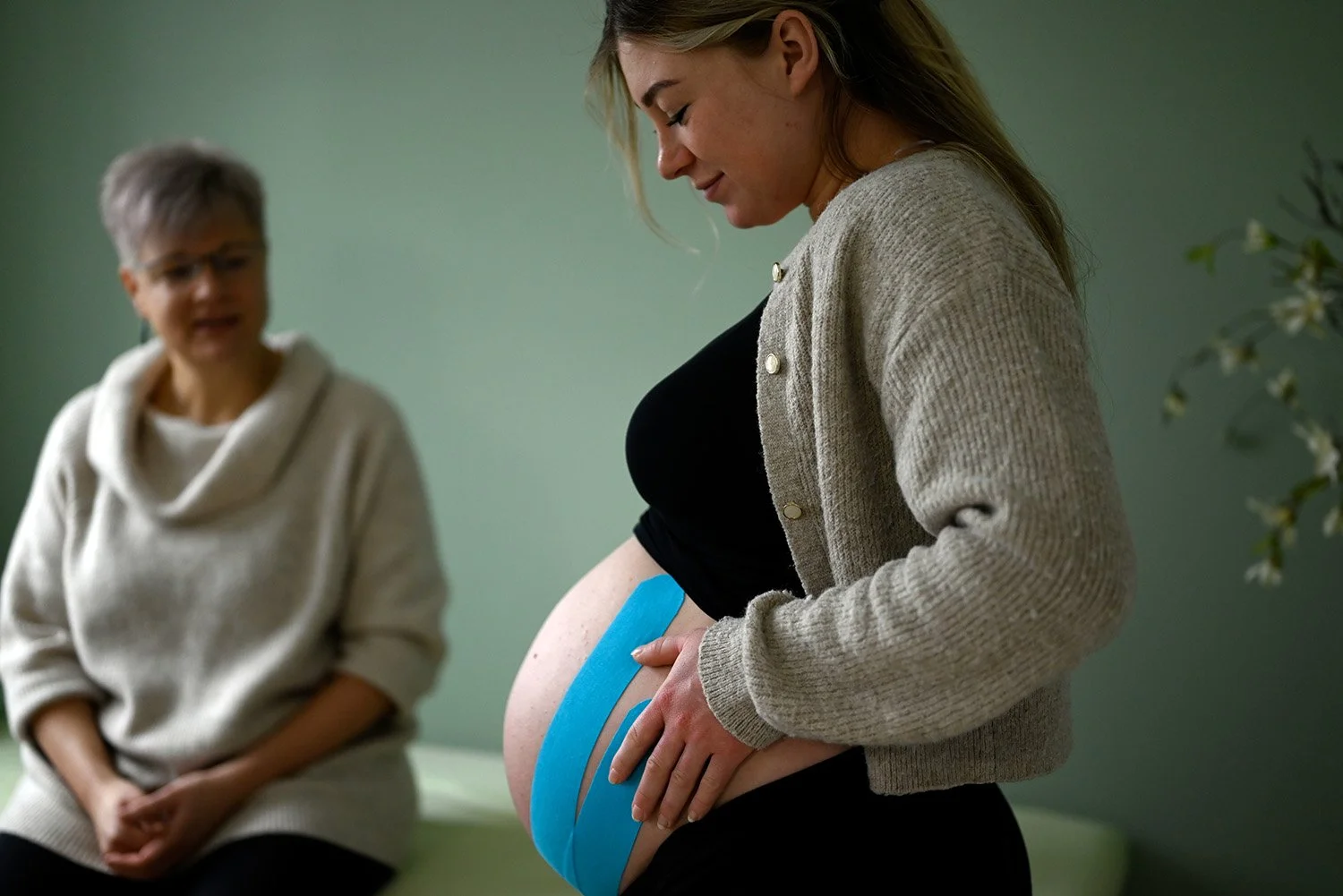 Schwangere betrachtet bei Hebammenvorsorge ihren Bauch mit Taping