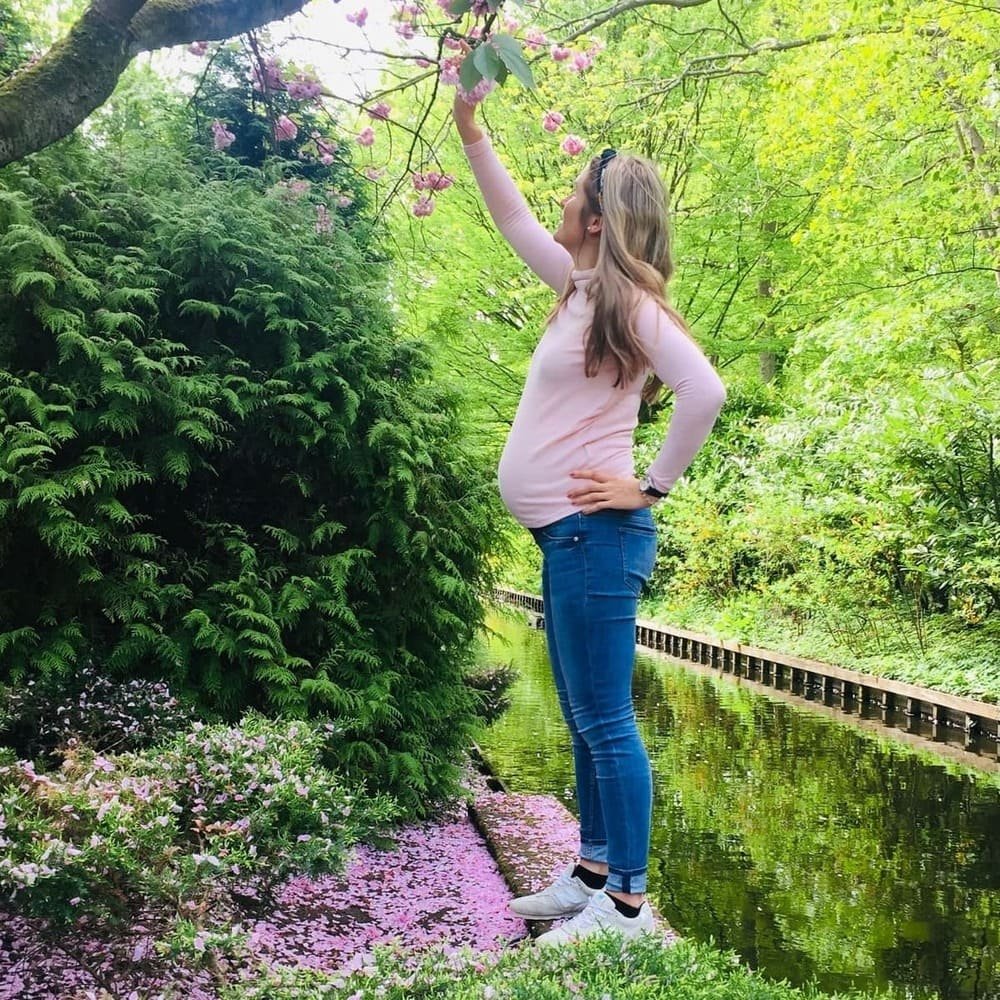 Schwangere Frau steht im Grünen und hält ihren Babybauch