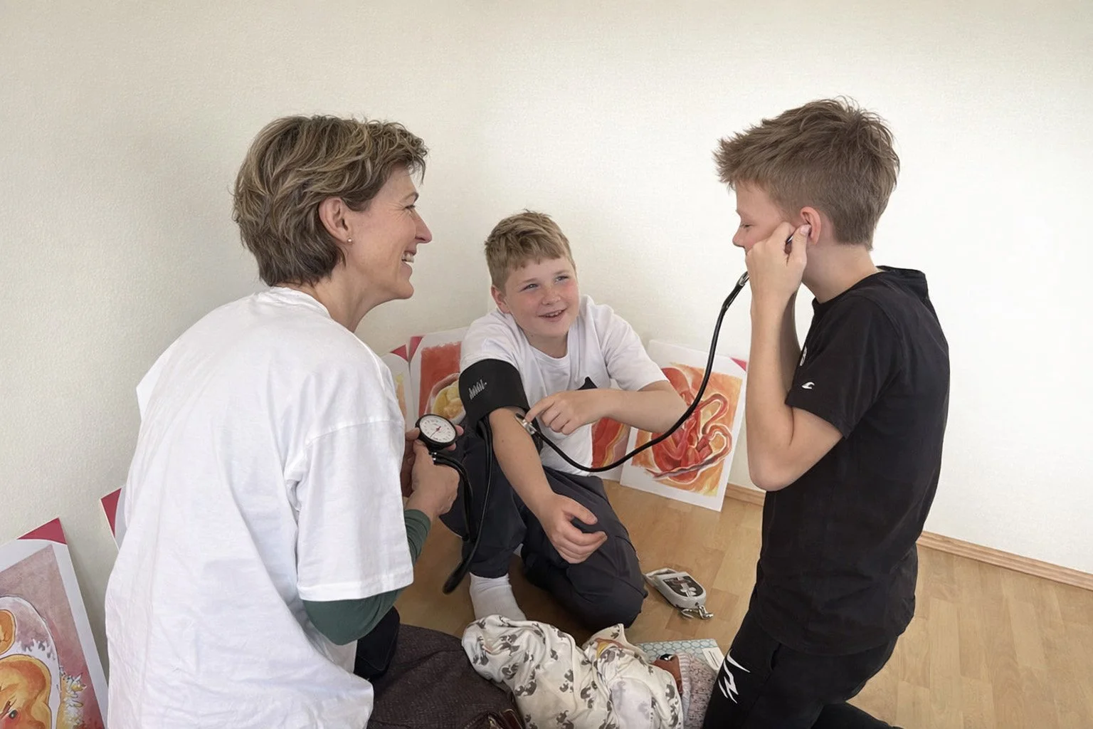 Hebamme erklärt 2 Jungs Blutdruckmessen. beide haben sichtlich Spaß an dieser Erfahrung