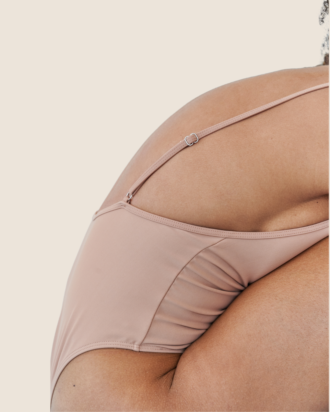 Close-up of a person's side with a beige slip dress, showing the shoulder and upper arm, against a plain light background.
