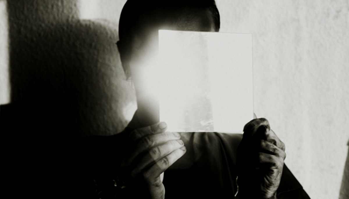 Person holding a blank sheet of paper in front of their face, obscuring their identity.