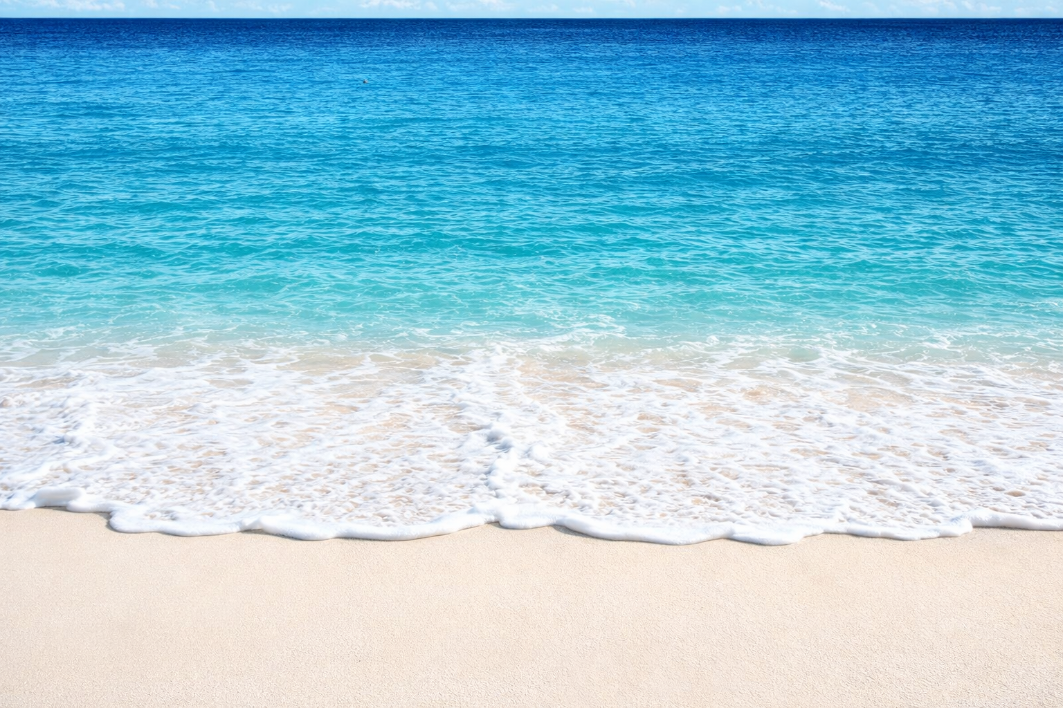 A peaceful beach with white sand and gentle waves lapping the shore, with clear blue ocean water and a blue sky.