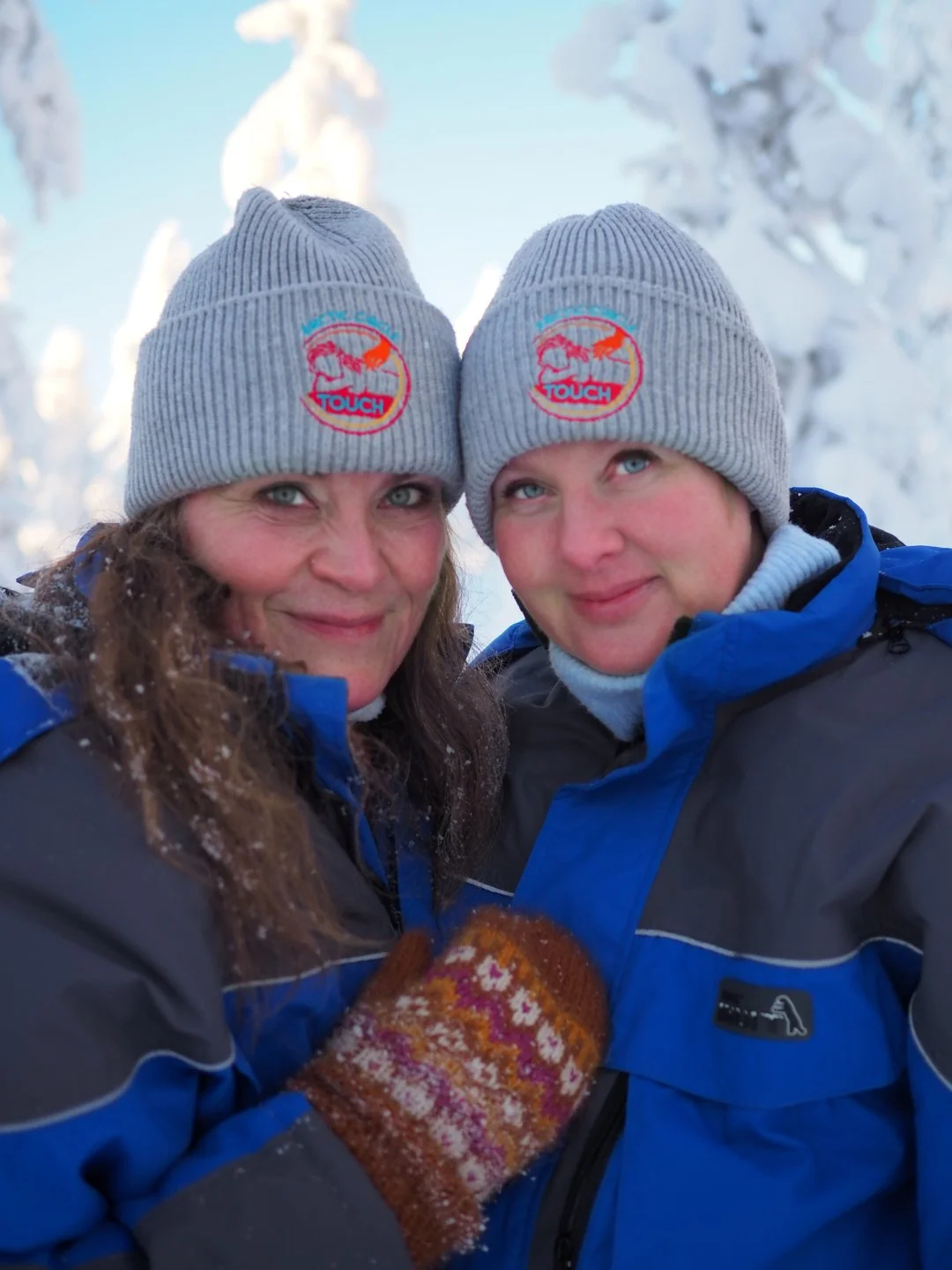 Kaksi ihmistä talvivaatteissa ja pipoissa, jotka poseeraavat lumisessa maisemassa.