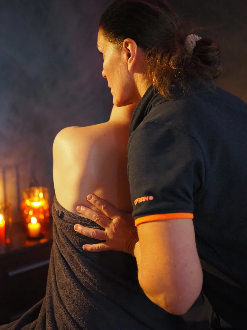 Nainen saa hierontaa selkäänsä hierojalta, huoneessa on kynttilöitä ja tunnelmavalo