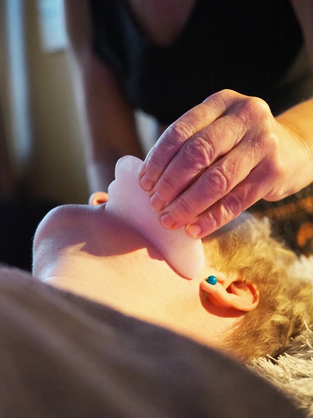 Ihmisen käsi antaa hierontaa päänahalle, jolla on panta ja korvakoru, lapsi makaa matolla.