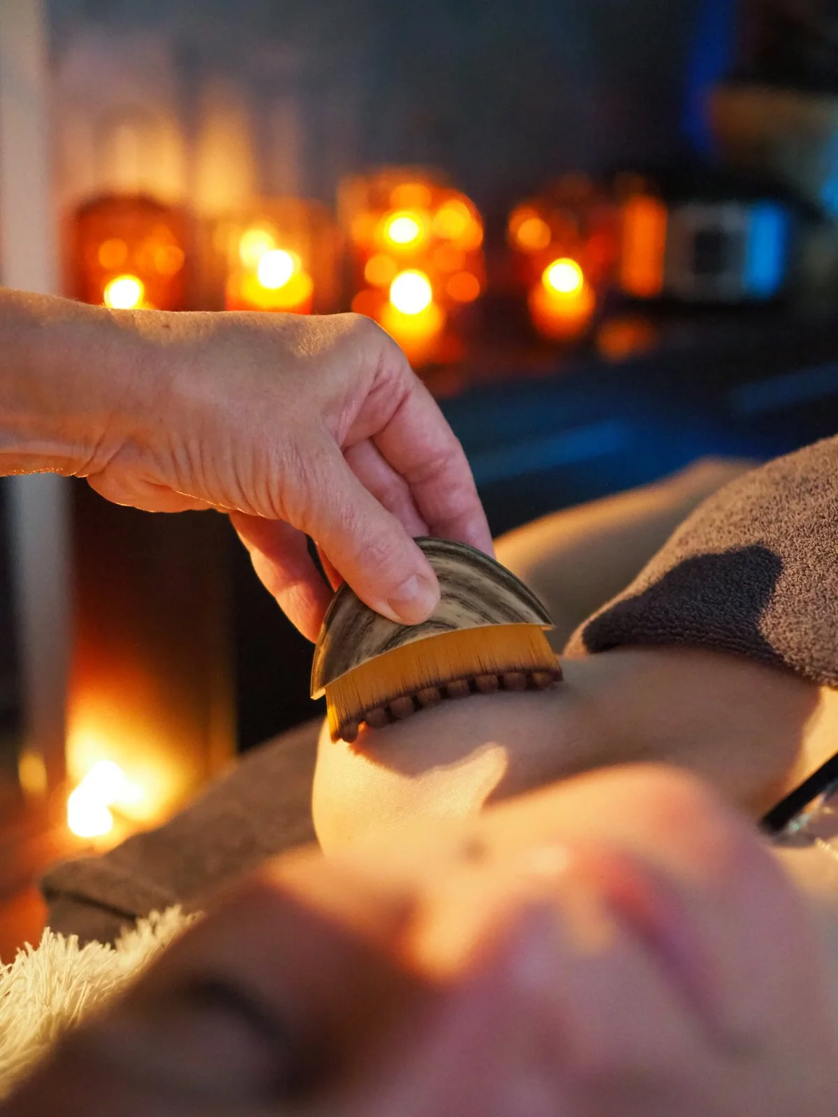 Kuva paikasta, jossa joku käyttää kuorintatyynyä ihon alueella. Taustalla palaa erilaisia kynttilöitä, luoden rentoa ja rauhallista tunnelmaa.