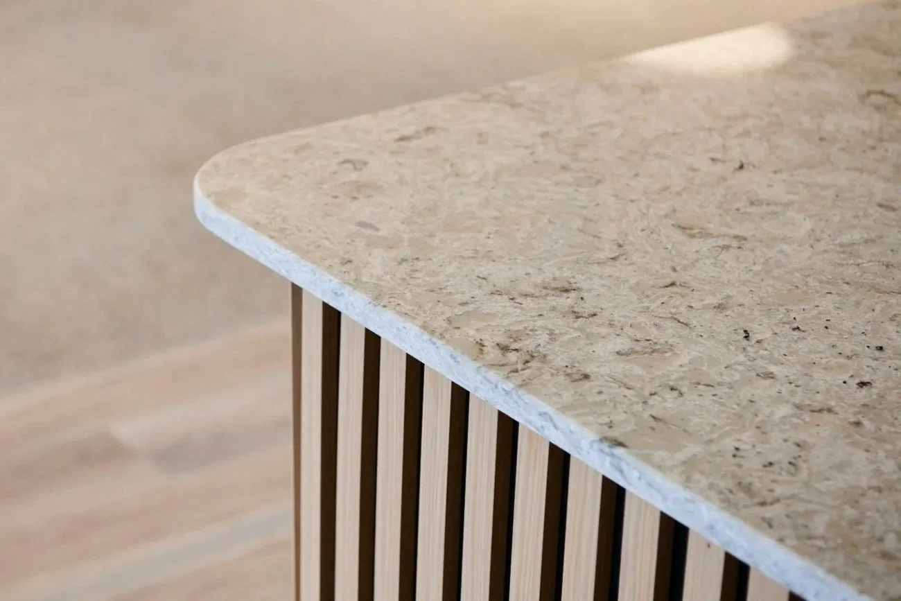 Close-up of a beige stone countertop with rounded edges, supported by a wooden slatted base.