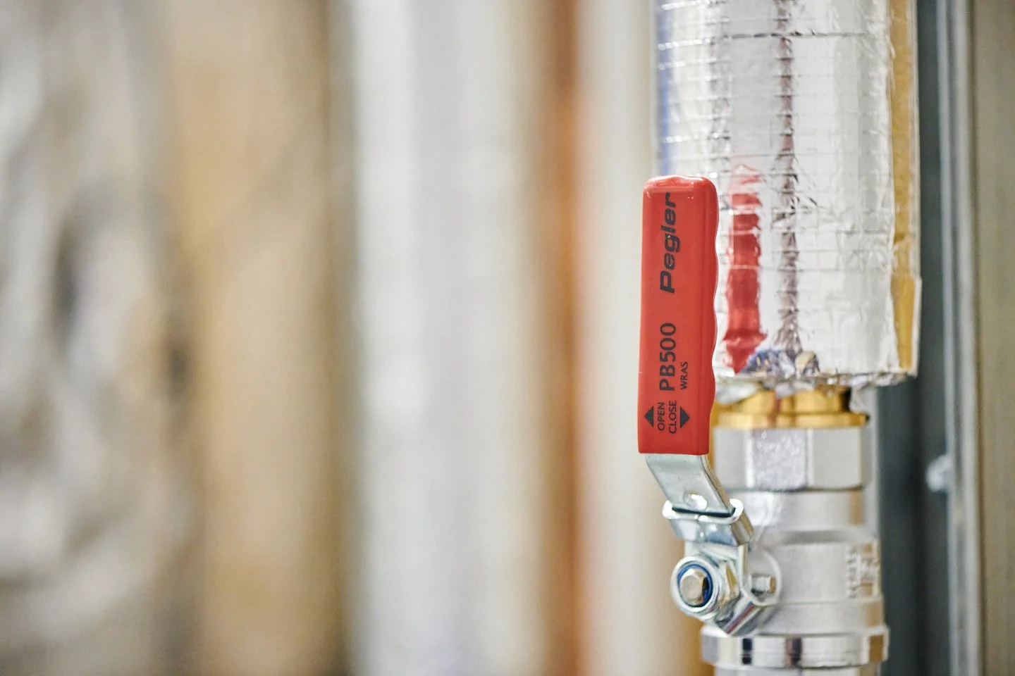 Close-up of a silver fire sprinkler with a red tag labeled 'Peger PB500' and the words 'Open Closes' with arrows indicating direction, mounted on a ceiling.