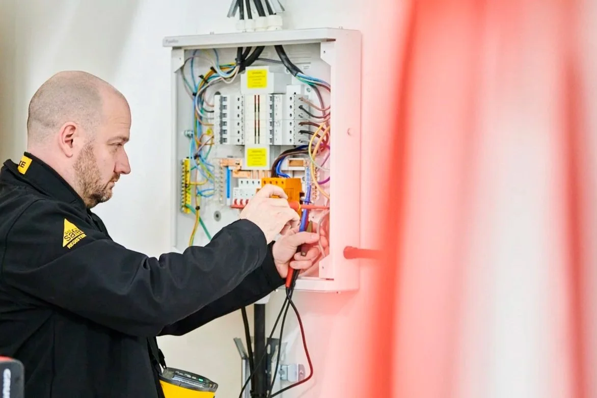 An electrician working on a wall-mounted electrical panel with various wires and circuit breakers.